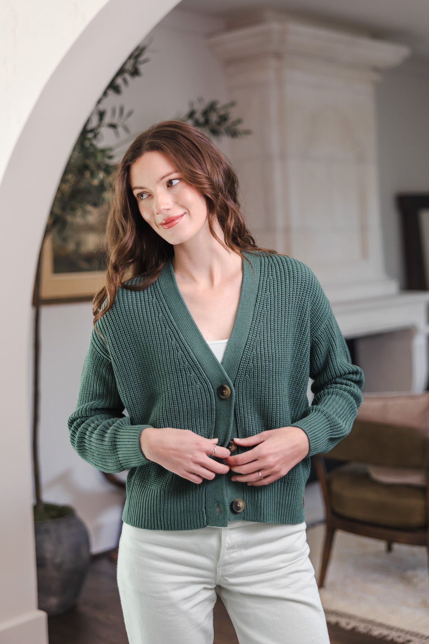 Modal standing in living room while wearing Chunky Knit Women's Cropped Cardigan in Pine over white pants