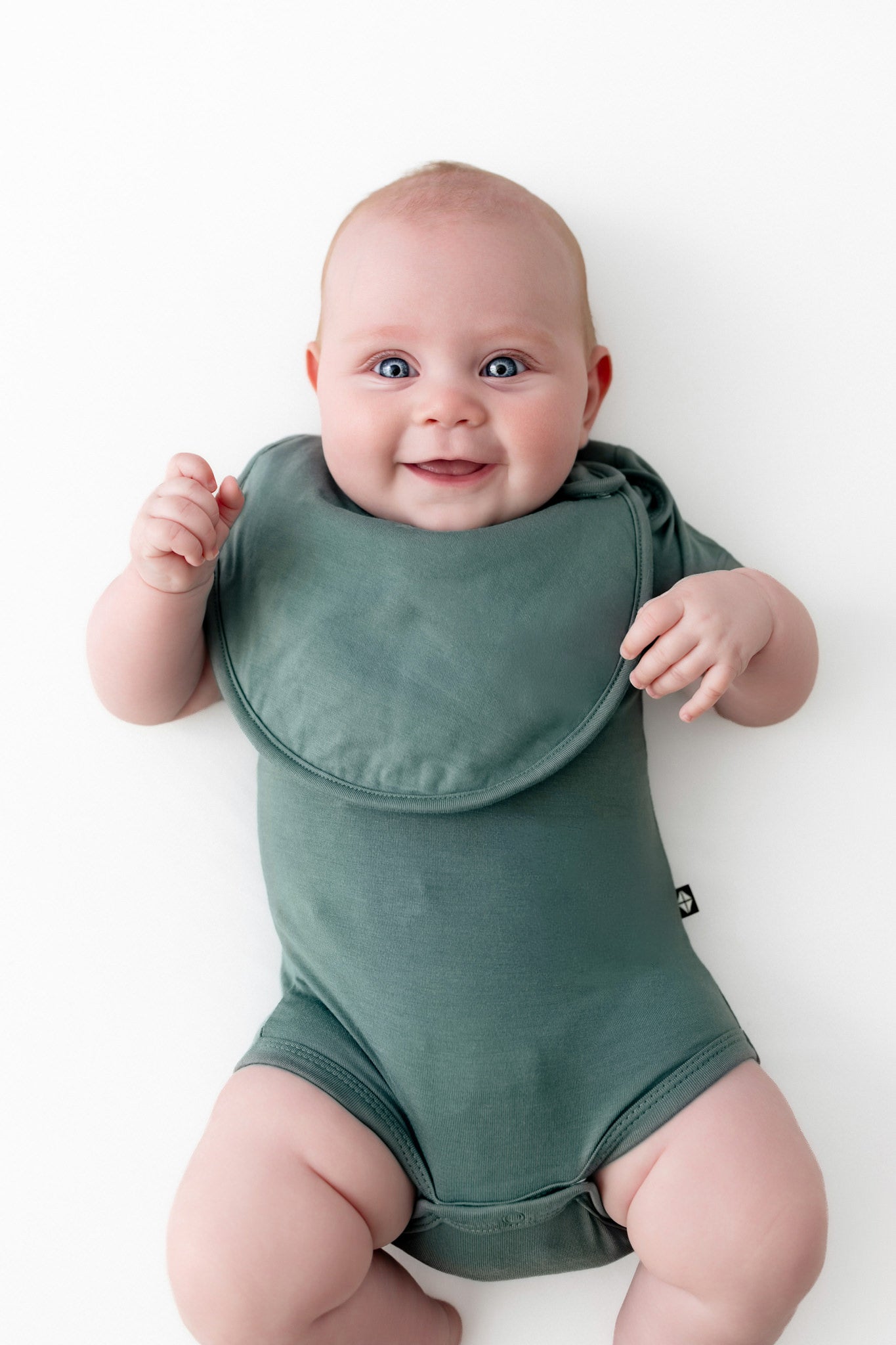 Baby wearing Cushy Bib in Pine over similar color bodysuit on a white background