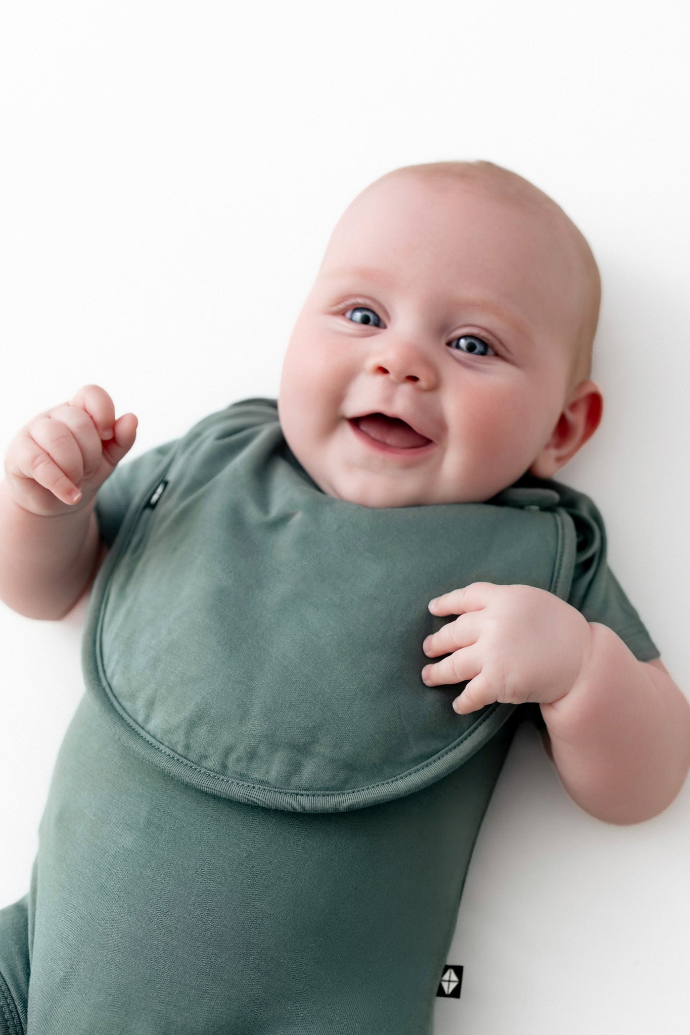Baby wearing Cushy Bib in Pine over similar color bodysuit on a white background