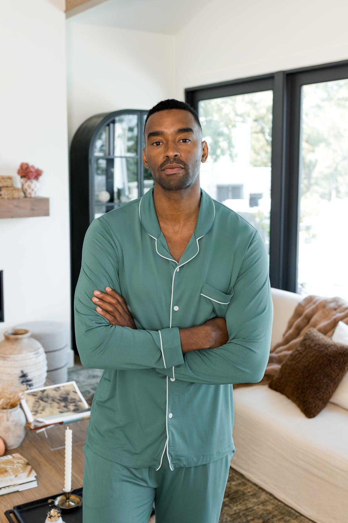 Model standing with folded hands in a living room wearing Men's Long Sleeve Pajama Set in Pine