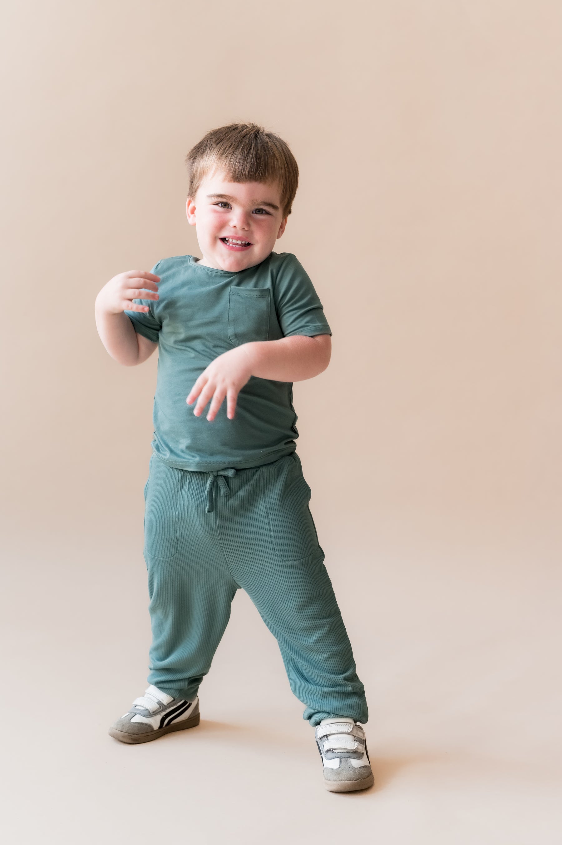 Child smiling in Ribbed Jogger Pant in Pine on a beige background