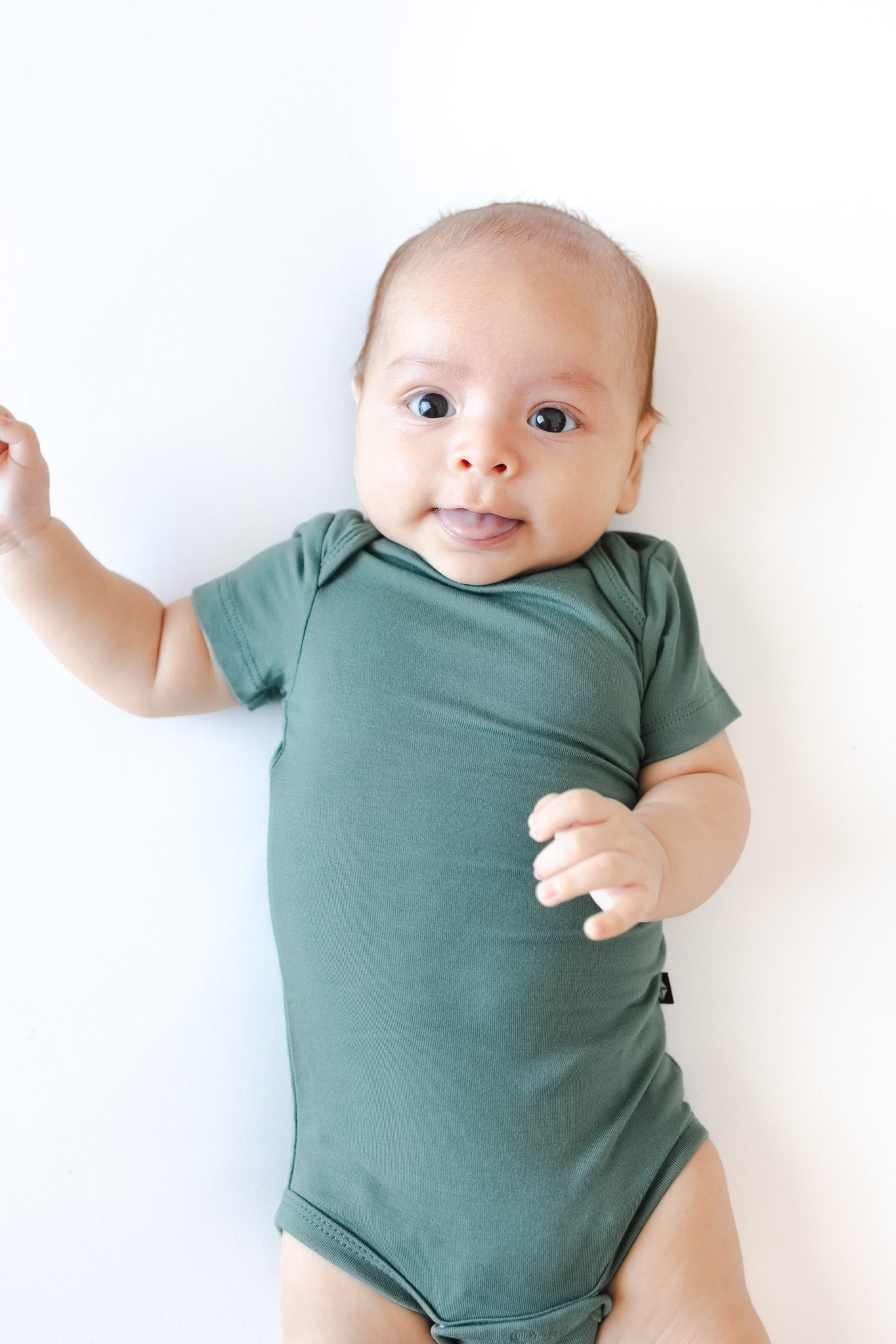 A baby wearing a sage green short-sleeve bodysuit, lying on a plain white background.