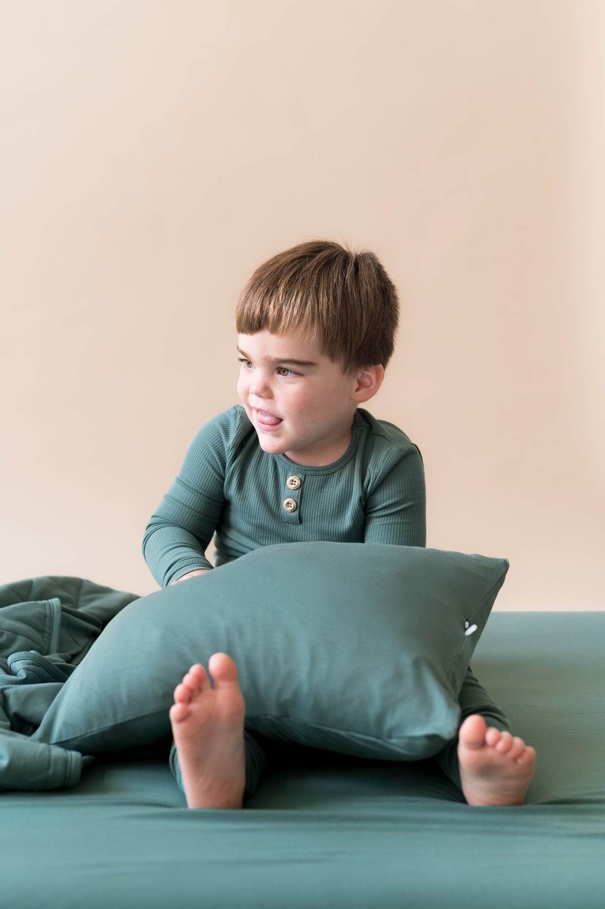Boy with Toddler Pillowcase in Pine wearing similar color shirt sitting on Pine sheet