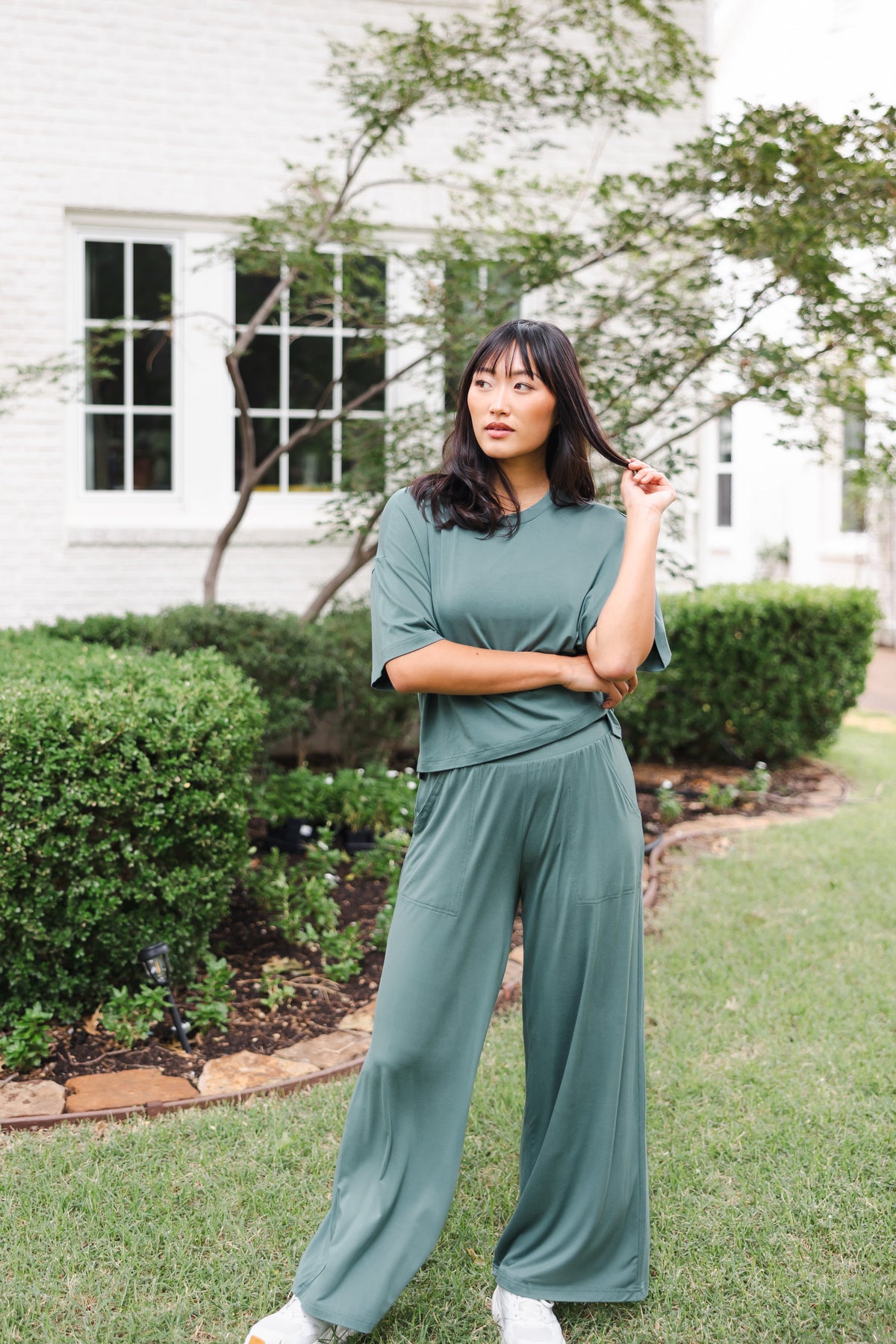Female model posing in garden outdoors wearing the Women's Wide Leg Pant in Burgundy and matching short sleeve tee on white shoes