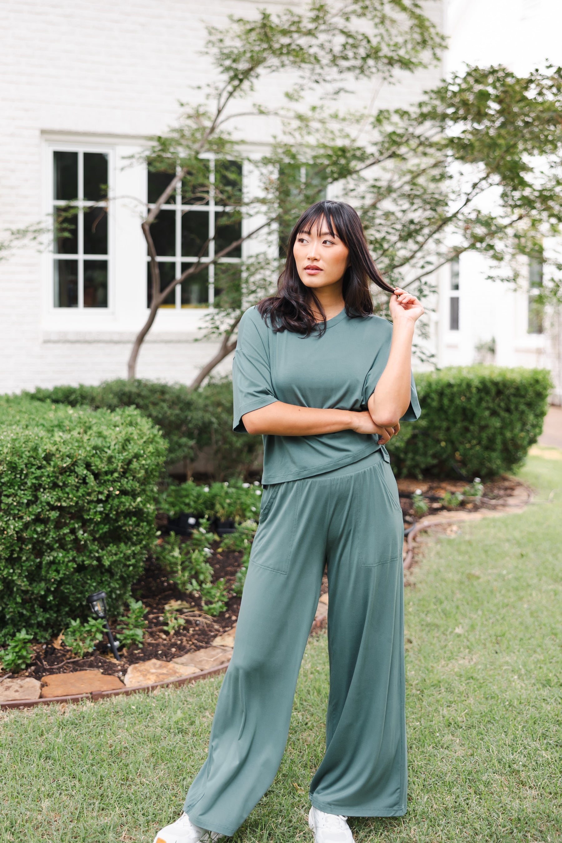 Female model posing in garden outdoors wearing the Women's Wide Leg Pant in Burgundy and matching short sleeve tee on white shoes