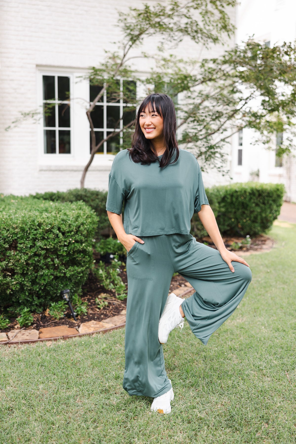 Female model smiling in a garden outdoors wearing the Women's Wide Leg Pant in Burgundy and matching short sleeve tee over white shoes