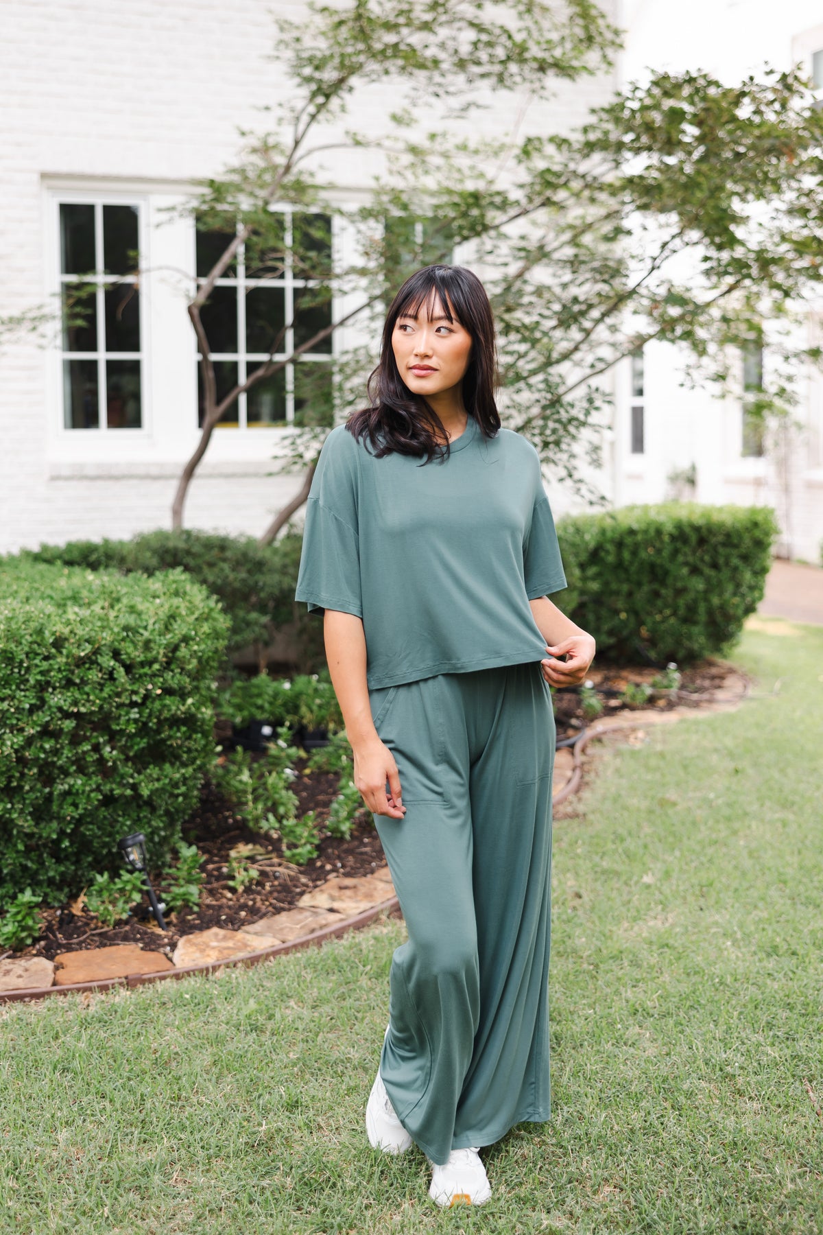 Female model posing in a garden outdoors wearing the Women's Wide Leg Pant in Burgundy and matching short sleeve tee over white shoes
