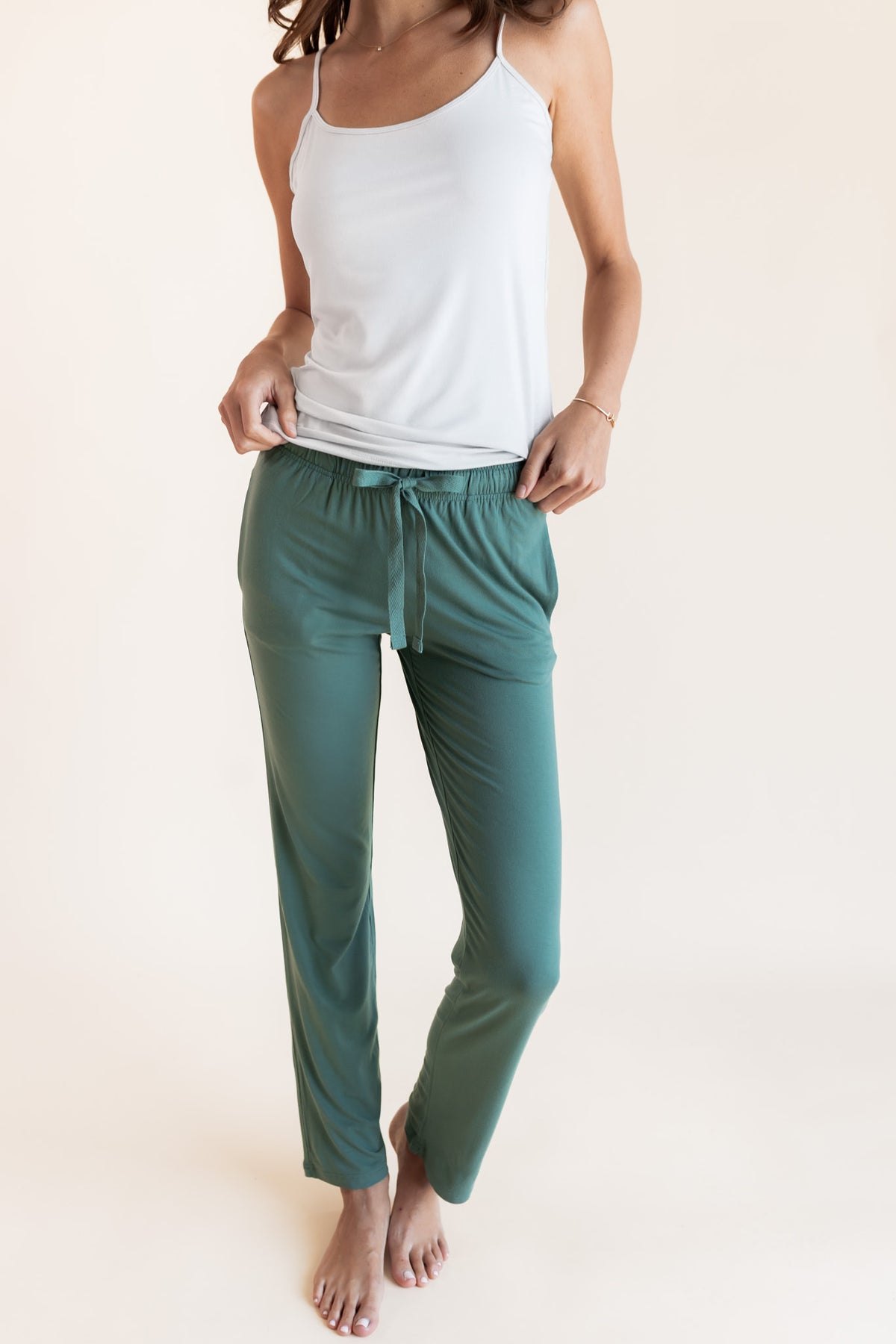 Model wearing Women's Lounge Pants in Pine under white camisole on a beige background