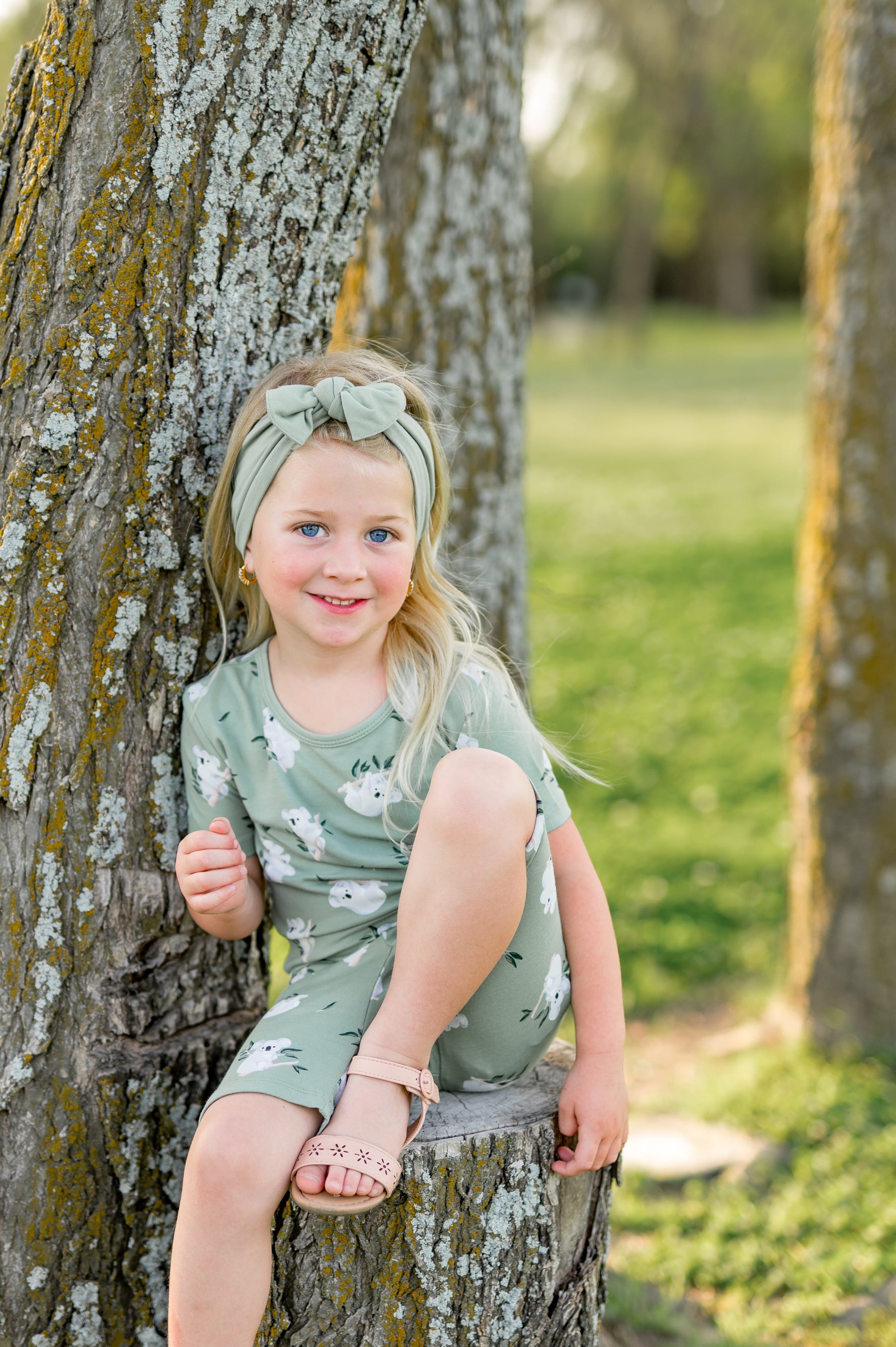 Young girl sitting on a tree stump beside a tree wearing the Short Sleeve Pajamas in Koala