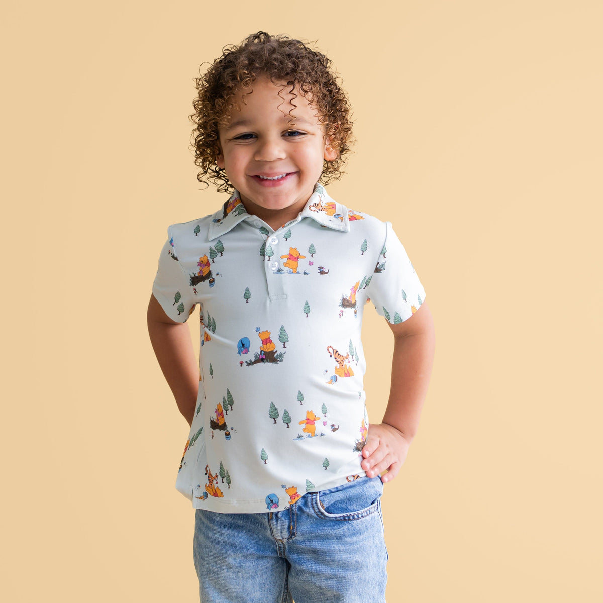 Smiling boy wearing the Toddler Short Sleeve Polo in Winnie the Pooh Hundred Acre Wood paired with jeans