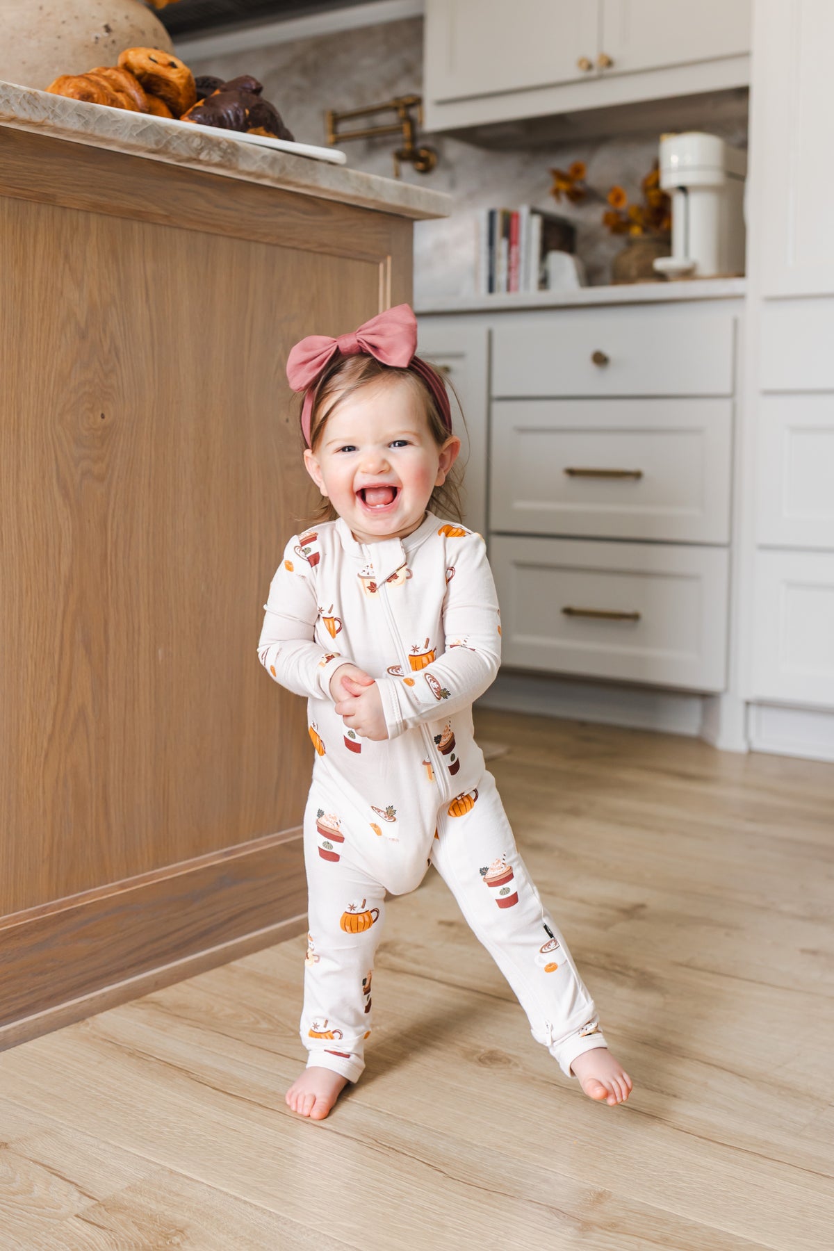 Toddler wearing Zippered Romper with Pumpkin Spice Latte print standing beside kitchen counter