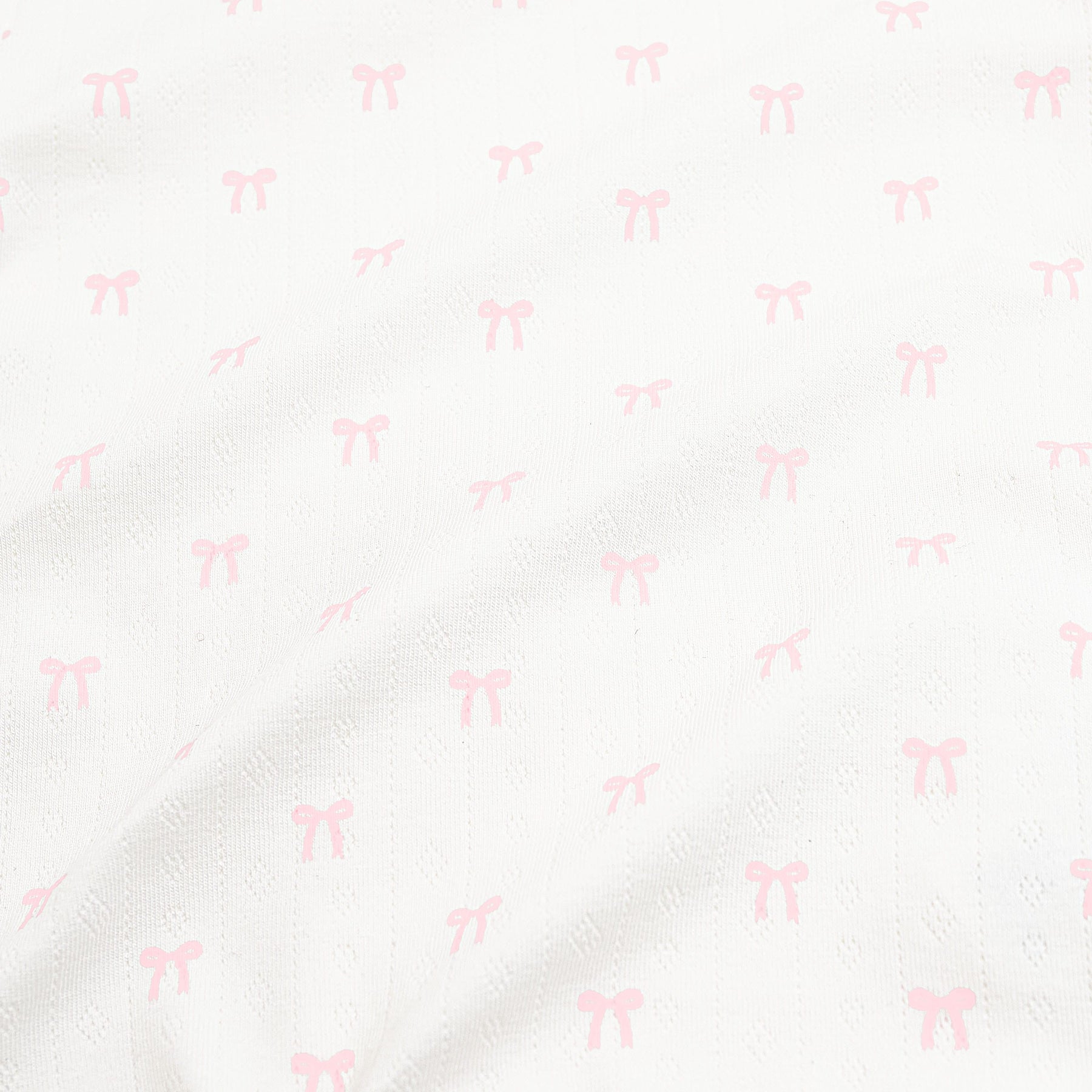 Close up of the pointelle fabric: An all-over print of dainty light pink bows over a white background.