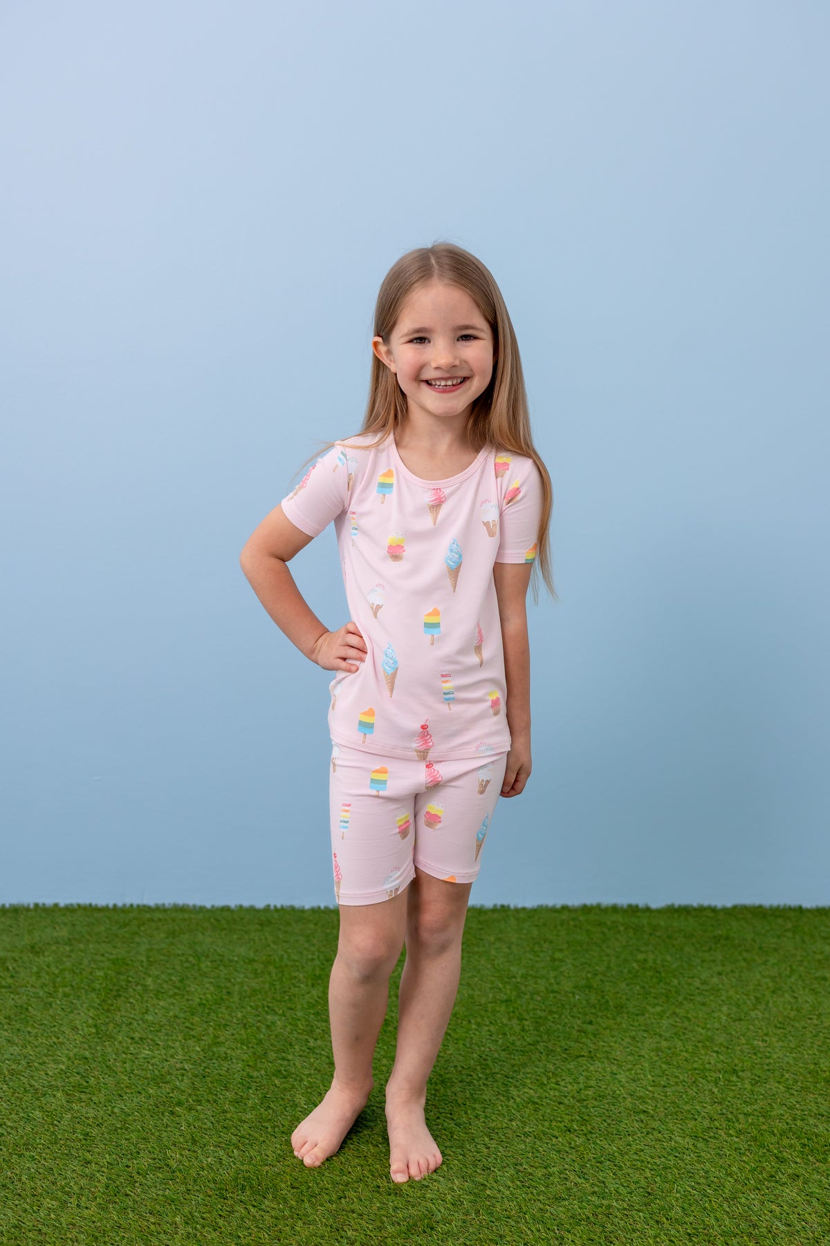 Child standing in Sakura Ice Cream print short sleeve pajama set on blue background and green grass
