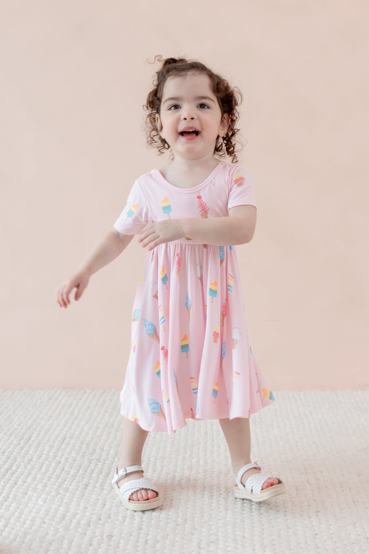 Child posing in Twirl Dress with Sakura Ice Cream print wearing sandles on a beige background