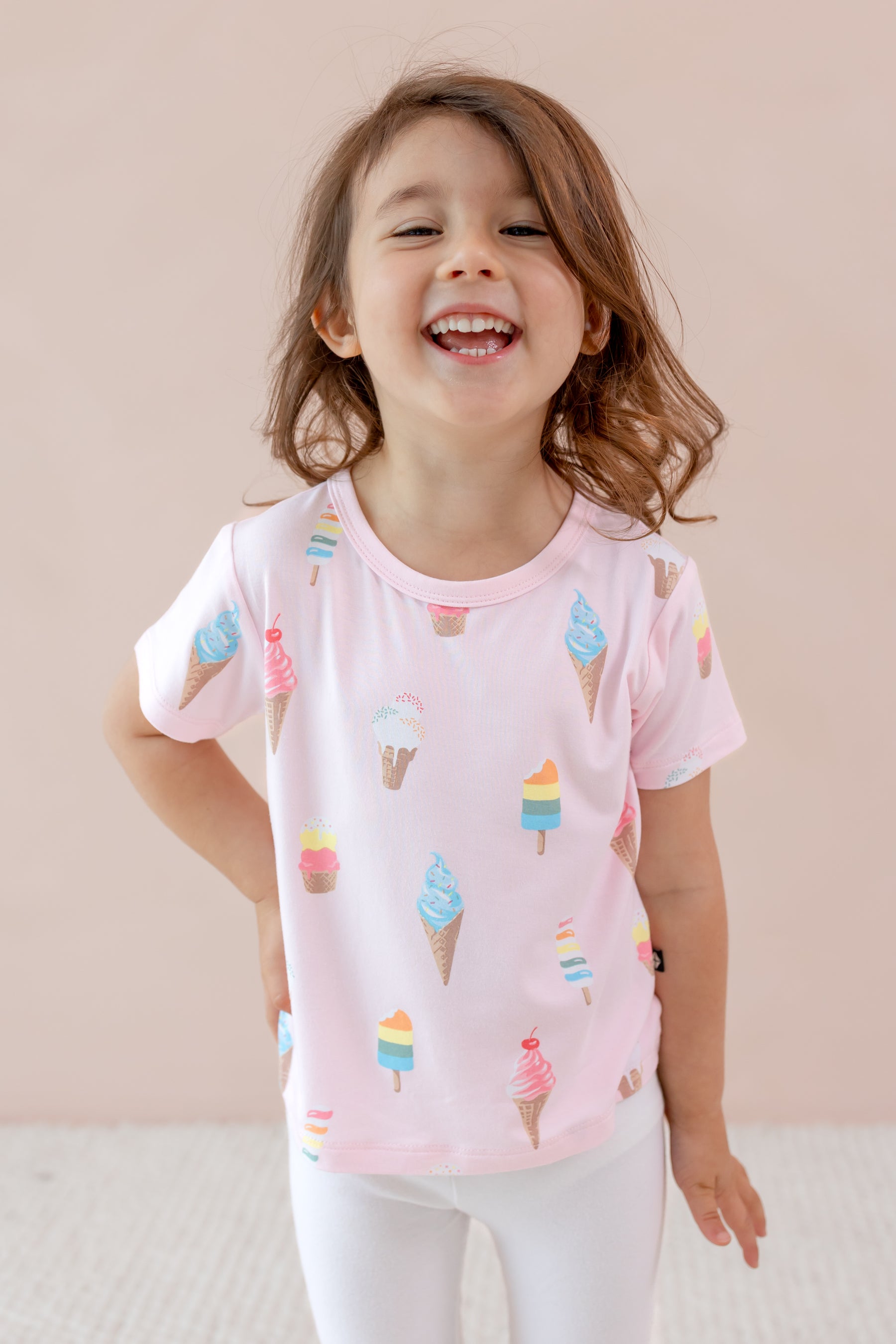 Child smiling in Toddler Basic Tee in Sakura Ice Cream print over white leggings on a beige background
