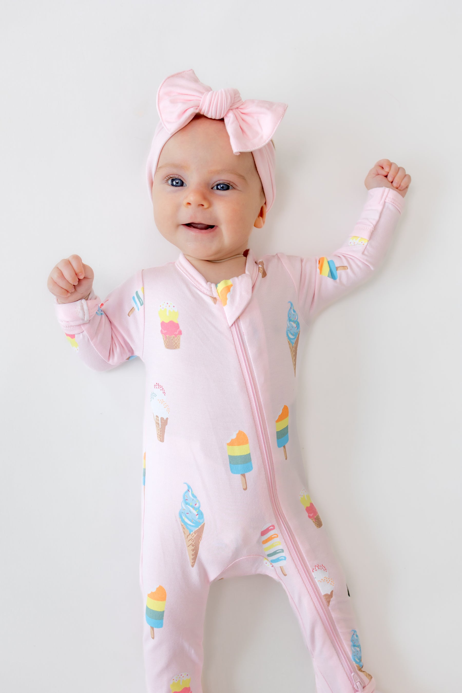 Baby in Sakura Ice cream print zippered footie with pink bow headband on a white background