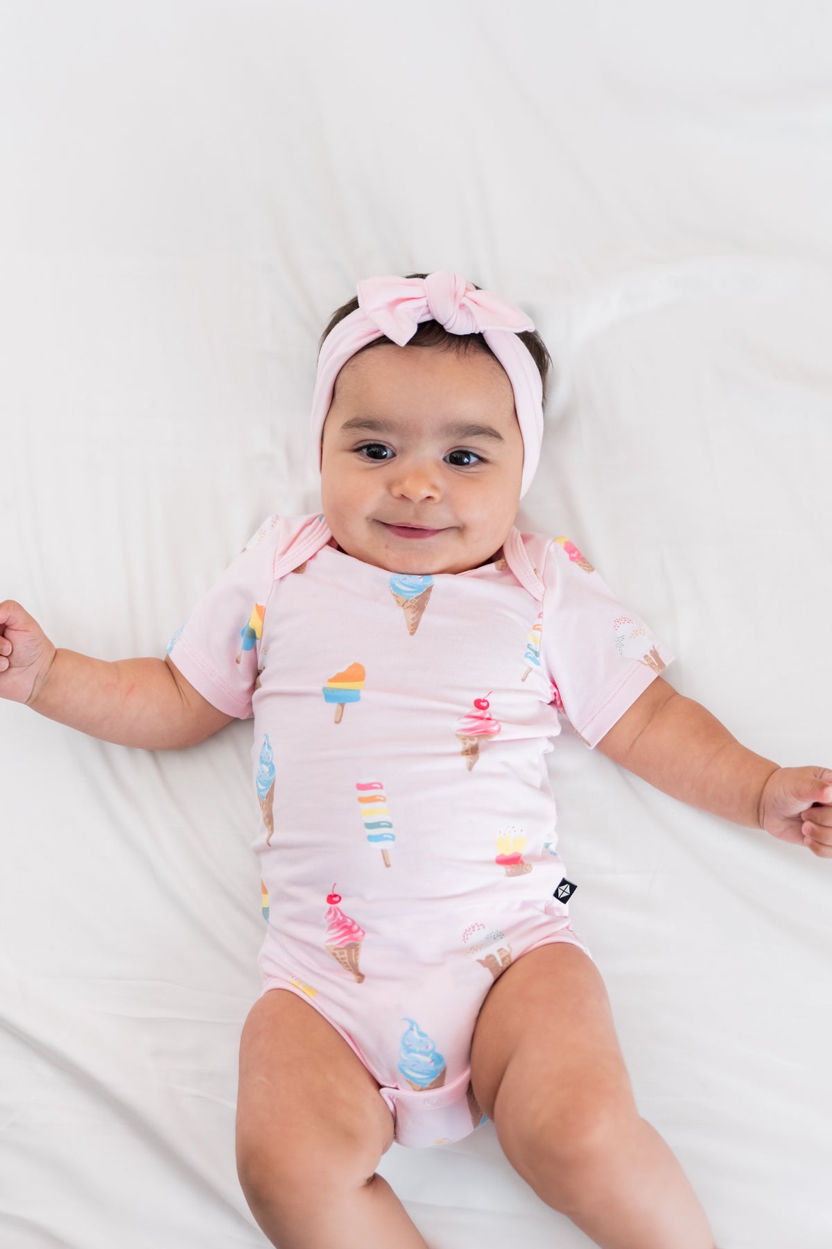 Baby wearing a Sakura Ice cream print Bodysuit with a pink bow headband on a beige background