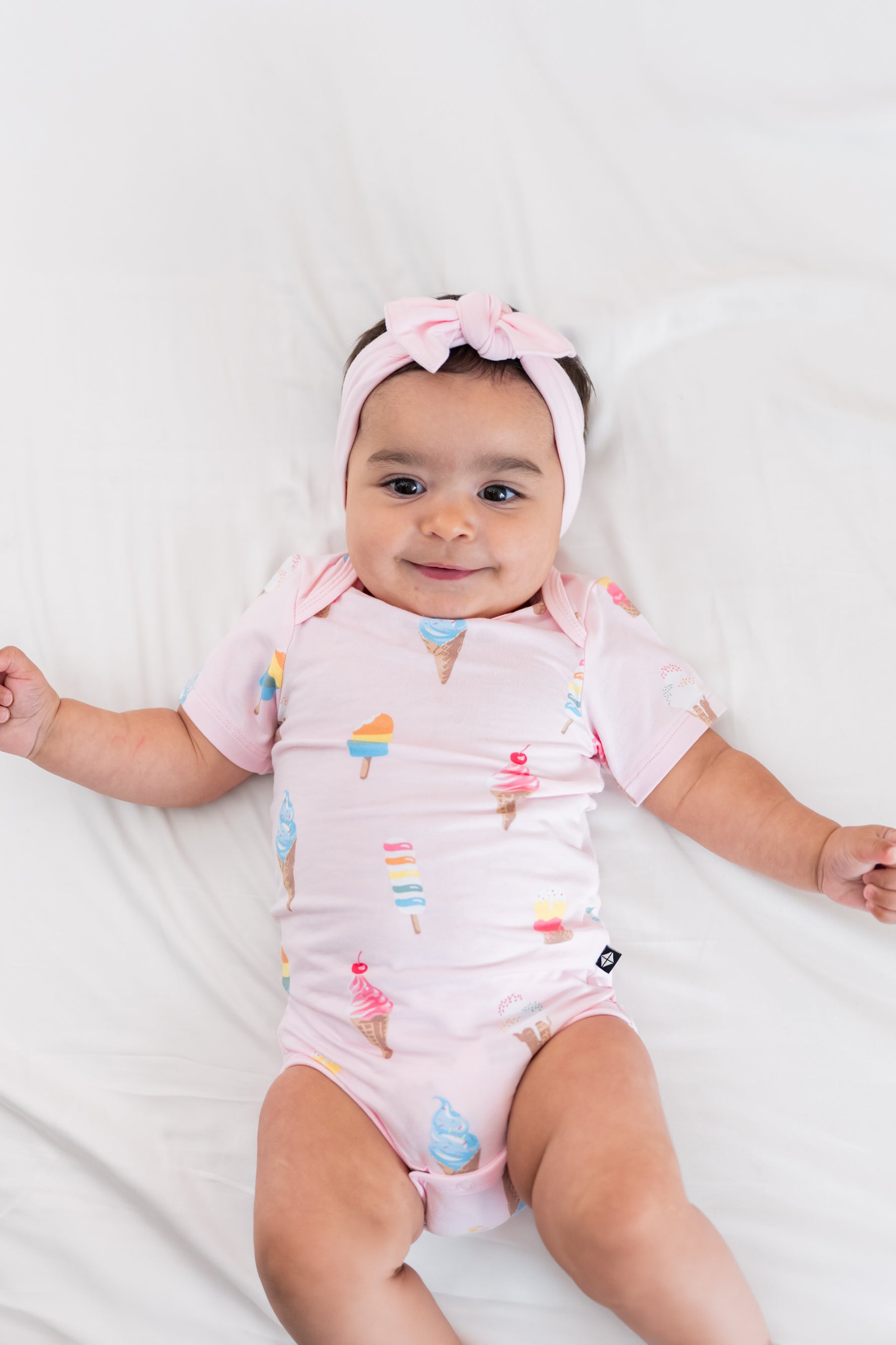 Baby wearing a Sakura Ice cream print Bodysuit with a pink bow headband on a beige background