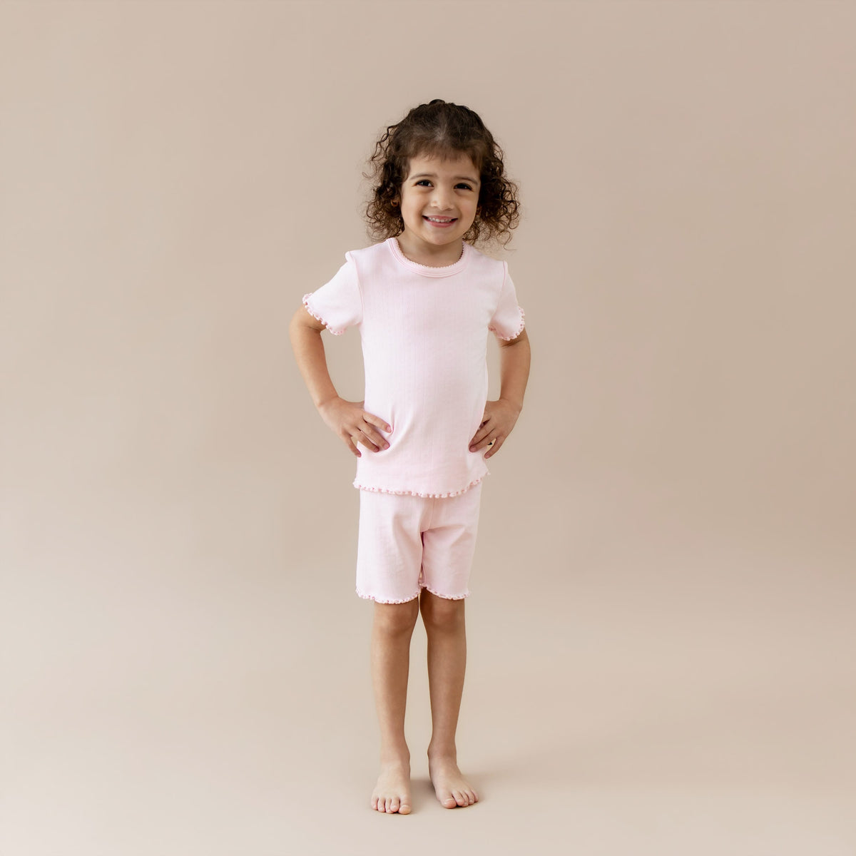 Child wearing a pink pointelle lounge outfit on a beige background