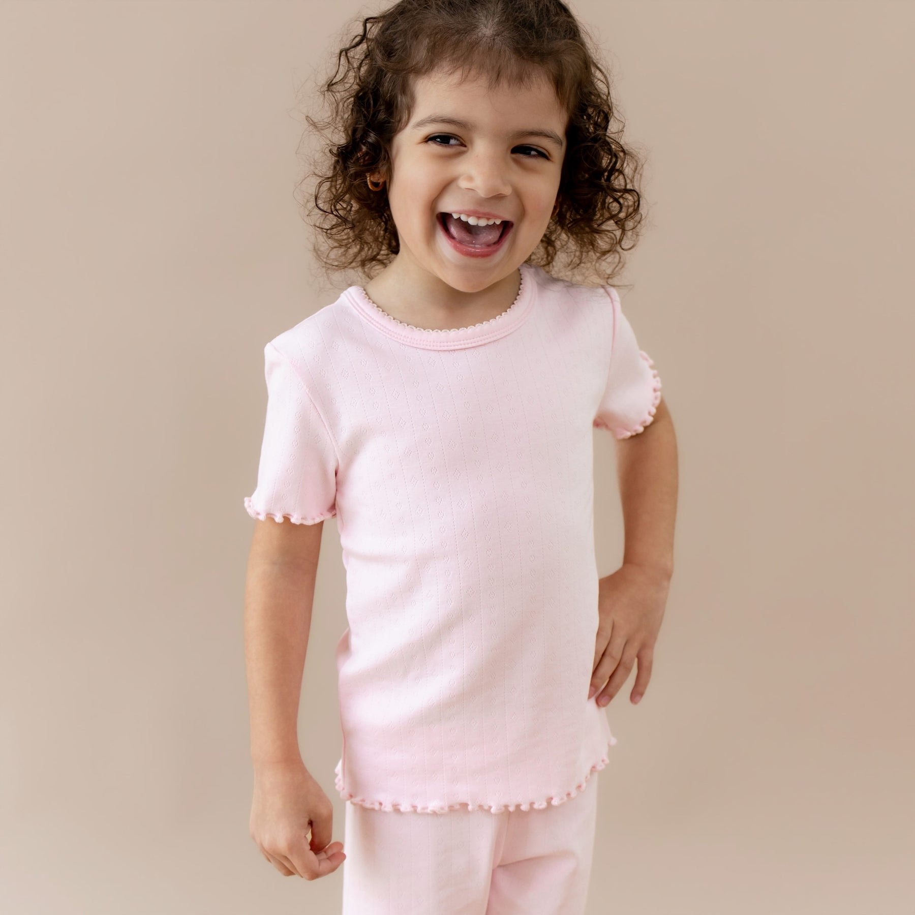 Child wearing a pink outfit with ruffled sleeves and hem on a beige background
