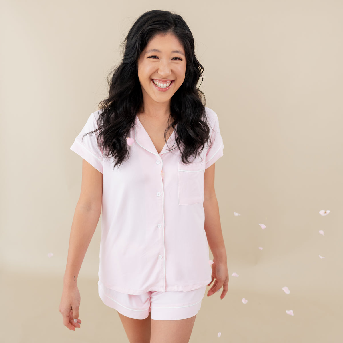 Woman modeling Women’s Short Sleeve Pajama Set in Sakura with Cloud Trim with rose petals falling around 