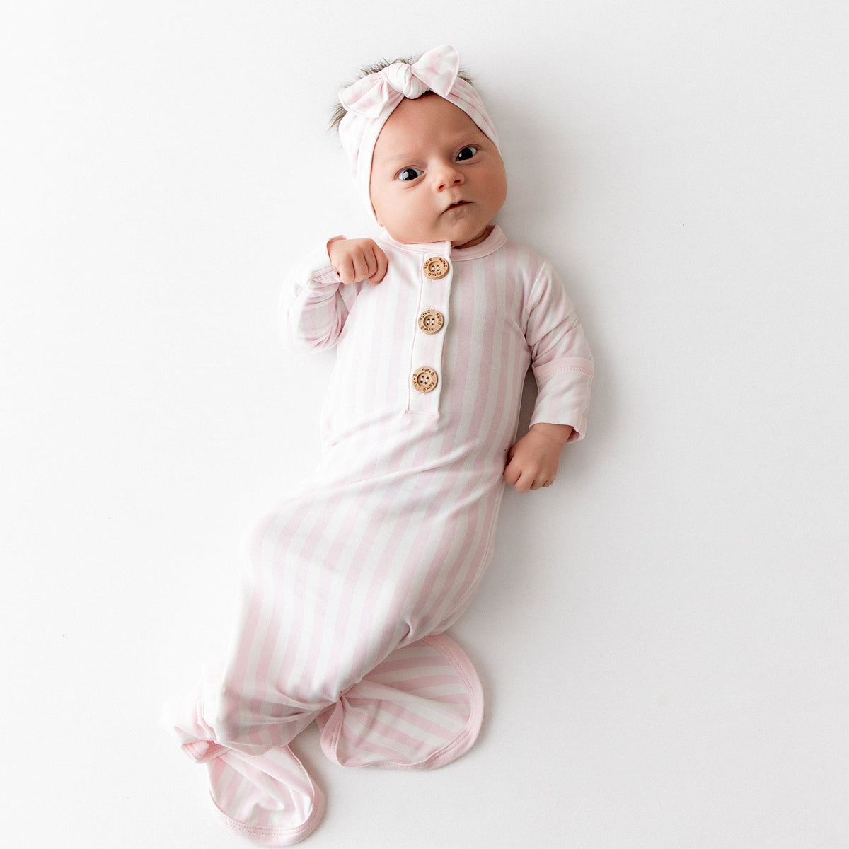Newborn laying on a white surface wearing the soft and breathable Knotted Gown with Bow Set in Small Sakura Stripe shown knotted