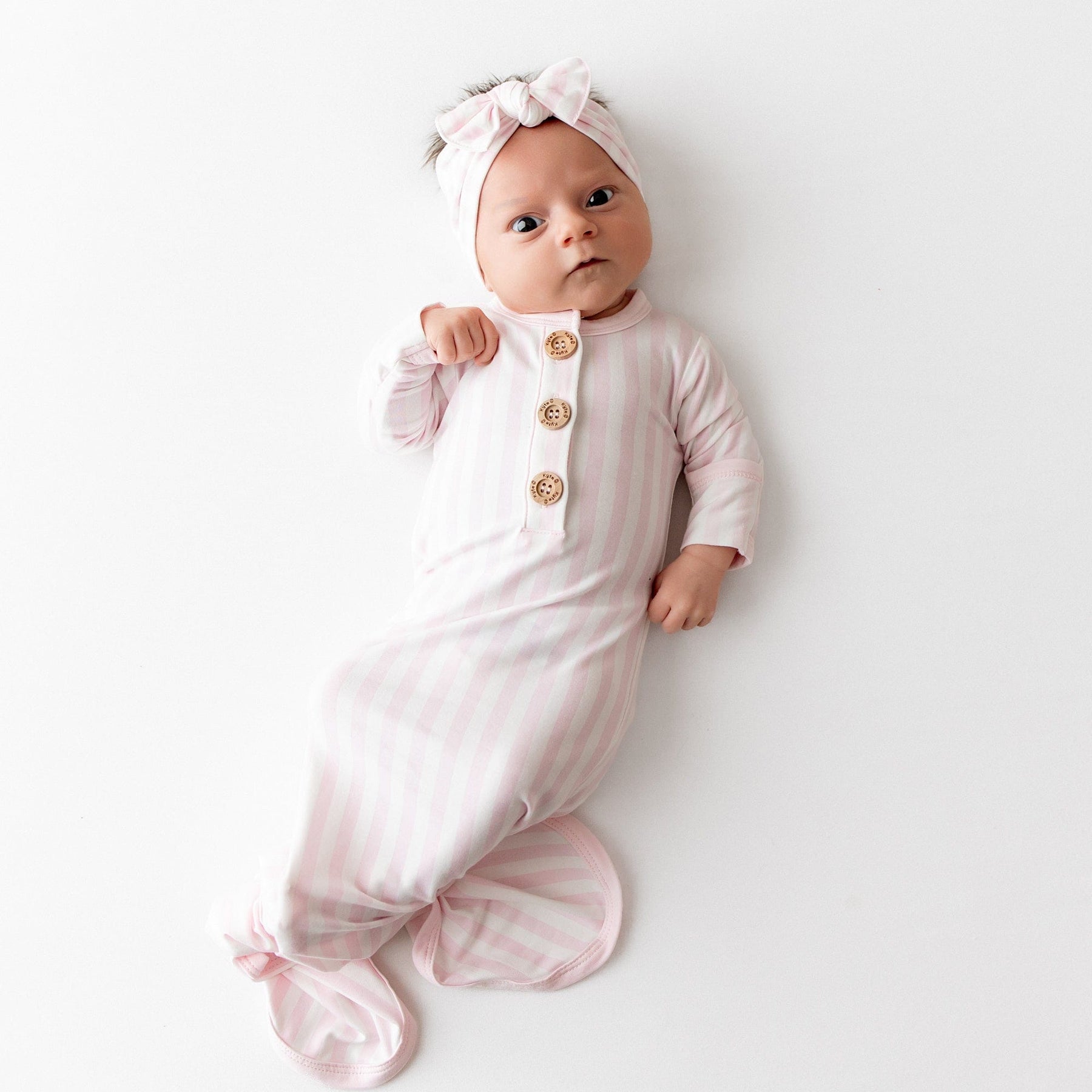 Newborn laying on a white surface wearing the soft and breathable Knotted Gown with Bow Set in Small Sakura Stripe shown knotted
