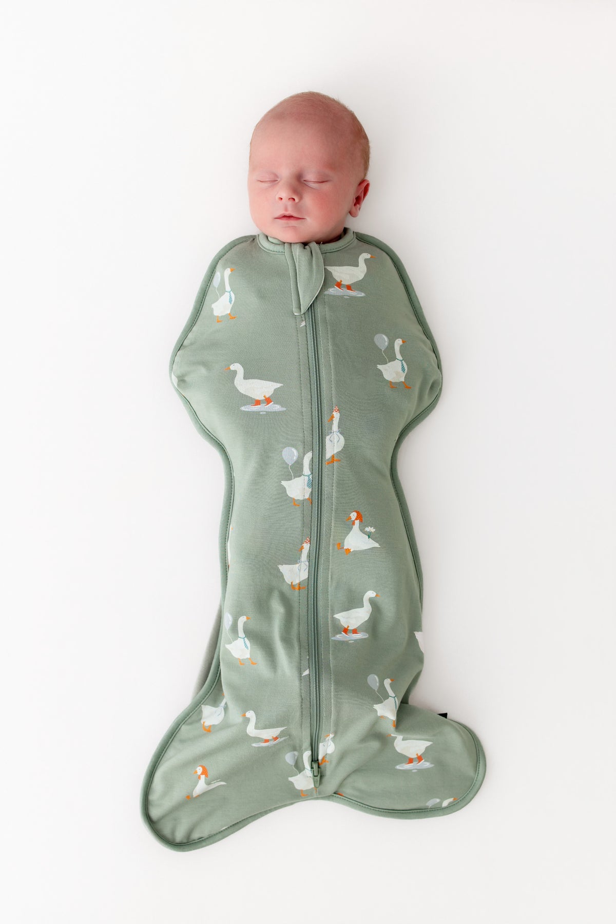 Baby sleeping in a green swaddle with goose pattern on a white background