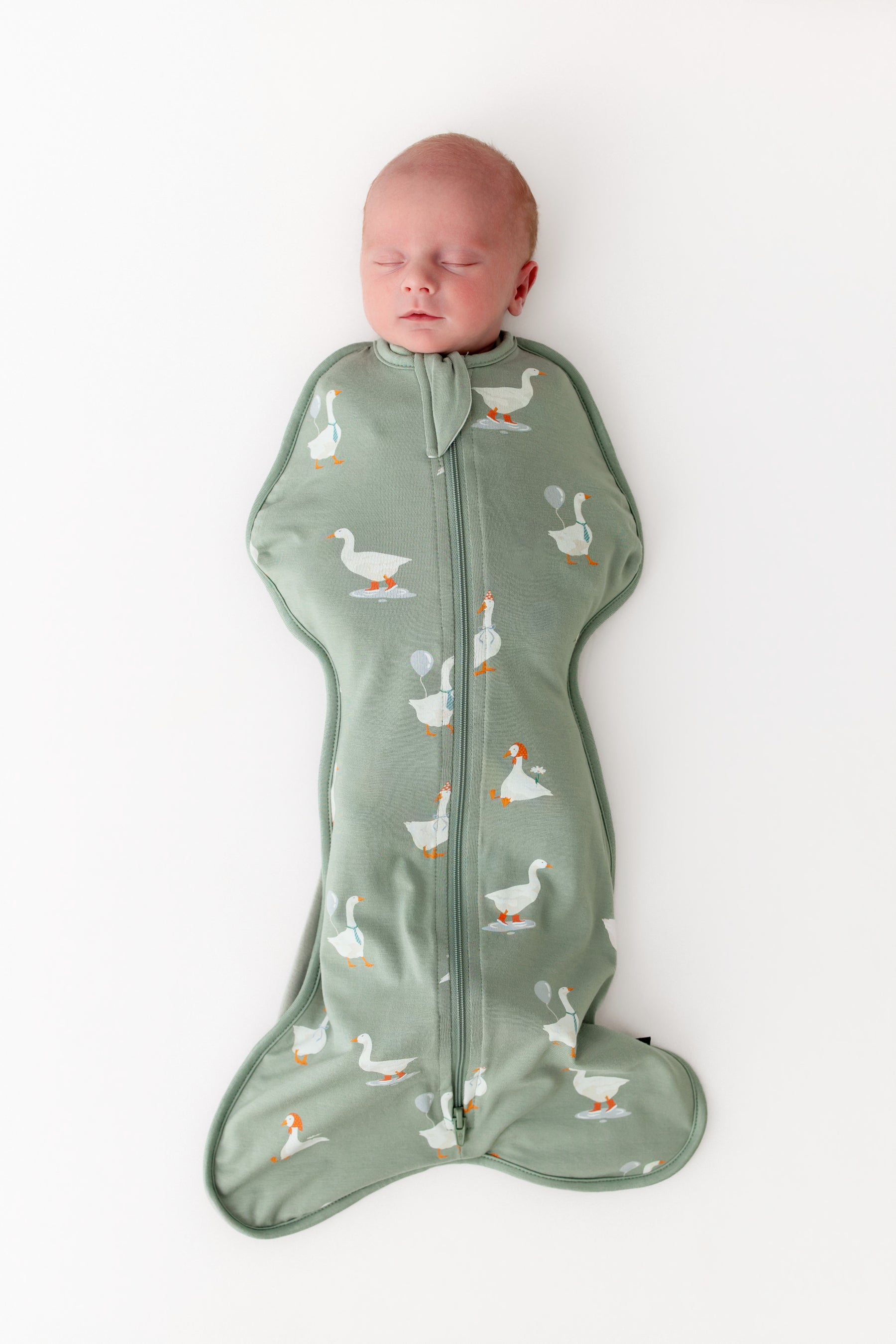 Baby sleeping in a green swaddle with goose pattern on a white background