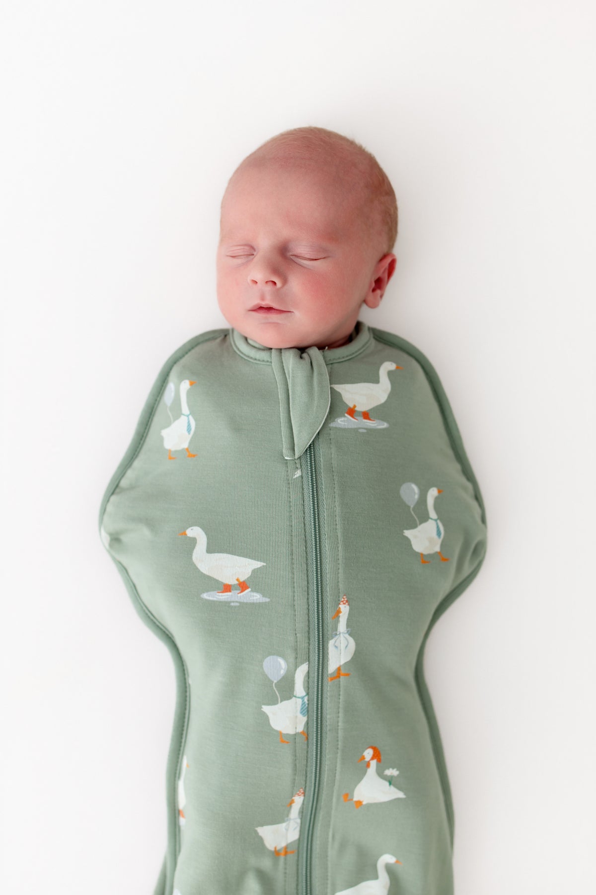 Newborn baby in a green swaddle with goose pattern on a white background
