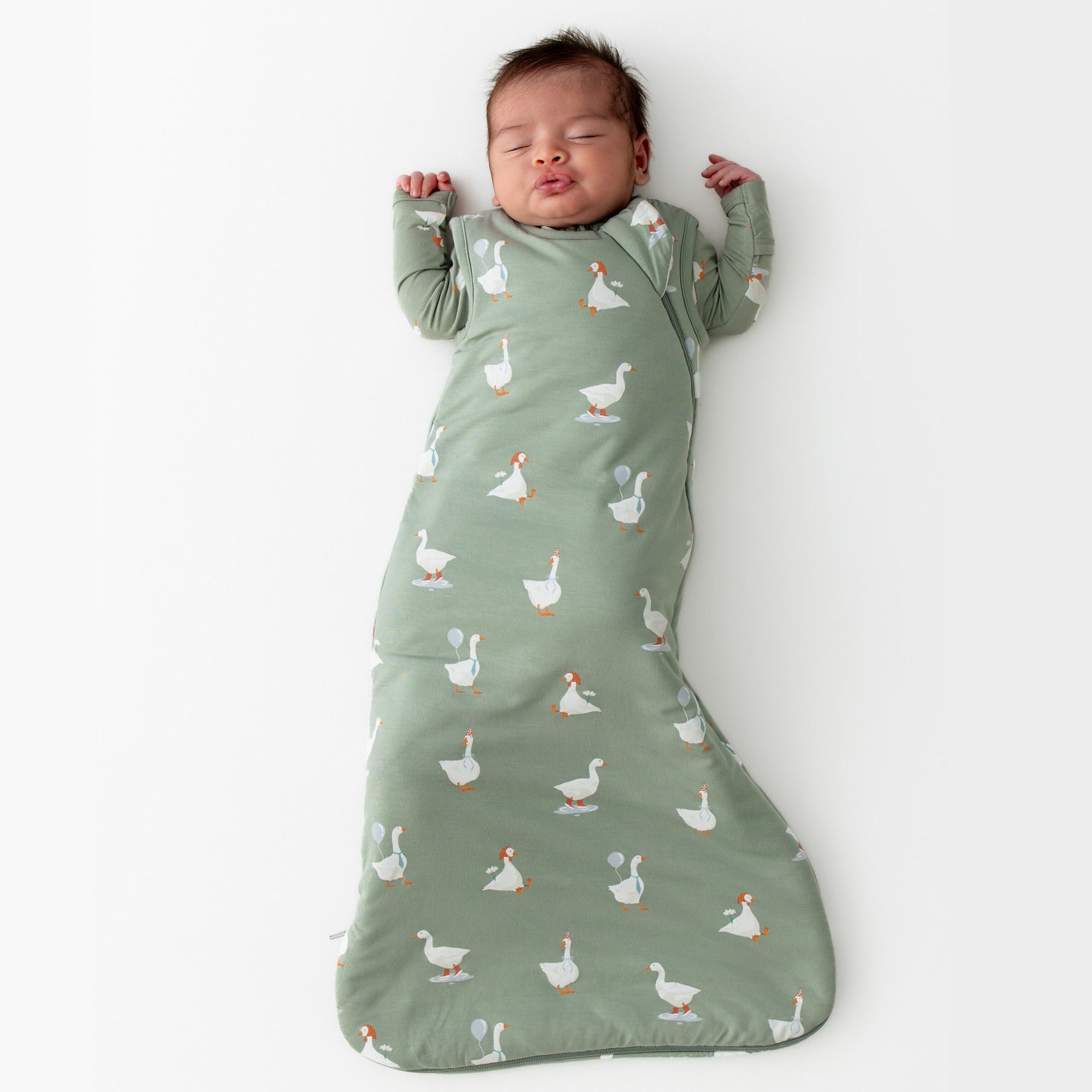 Baby asleep in a green sleep sack with a silly goose pattern on a white background
