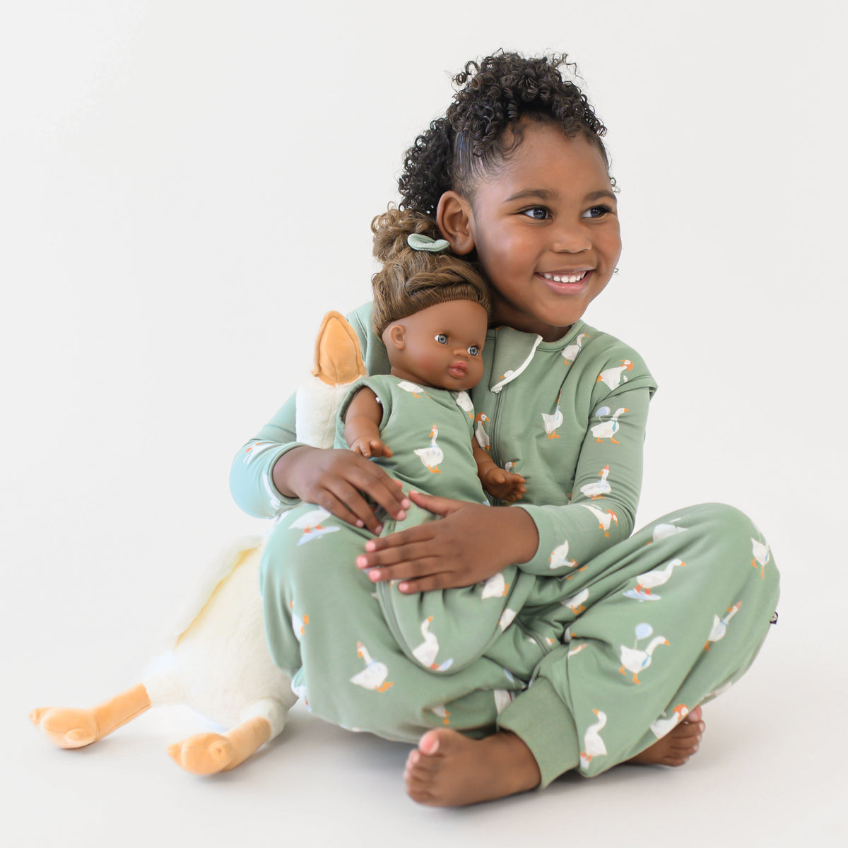 Young girl sitting wearing the long sleeve toddler pajamas and sleep bag walker in Silly Goose holding a doll who is wearing the Baby Doll Sleep Bag in Silly Goose 