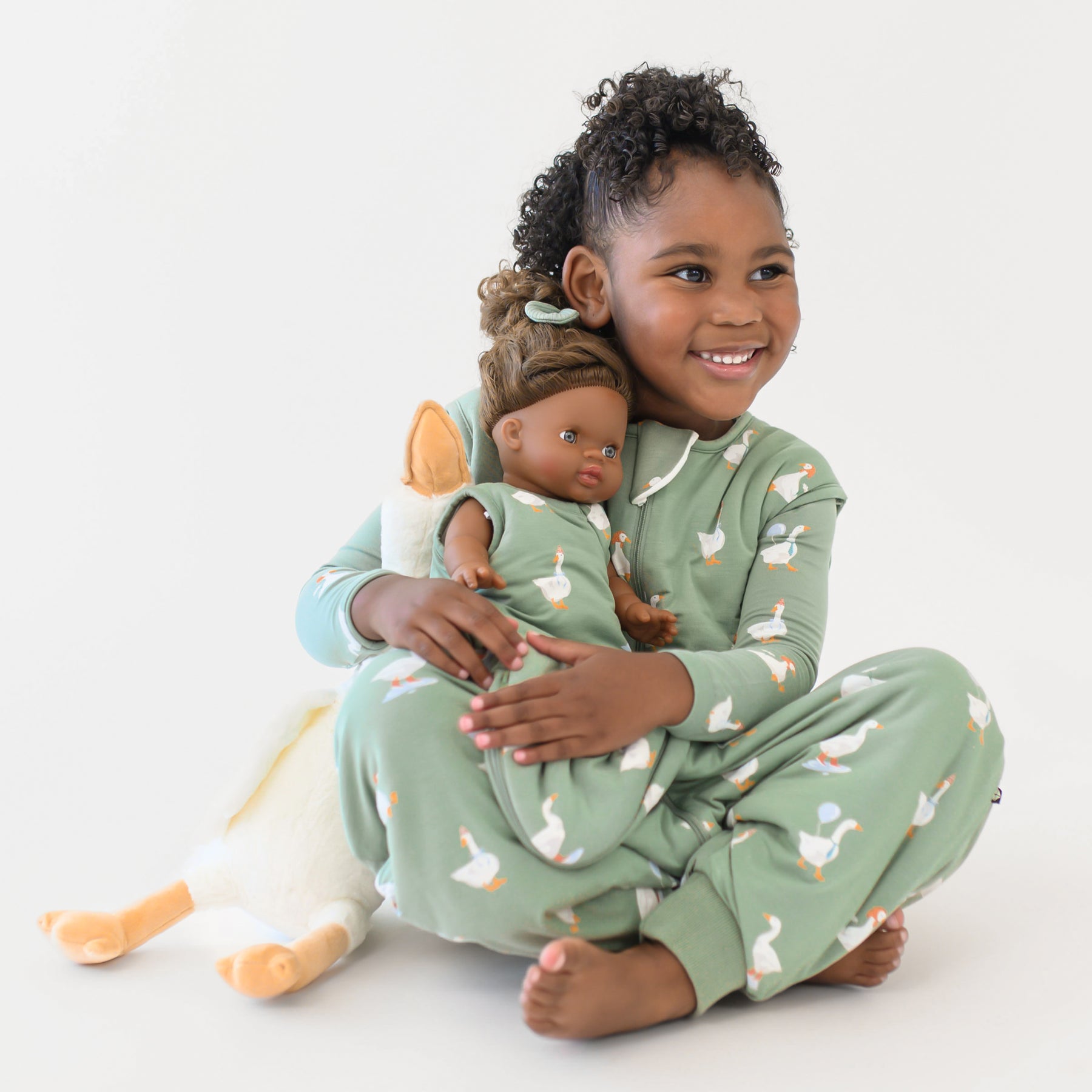 Young girl sitting wearing the long sleeve toddler pajamas and sleep bag walker in Silly Goose holding a doll who is wearing the Baby Doll Sleep Bag in Silly Goose 