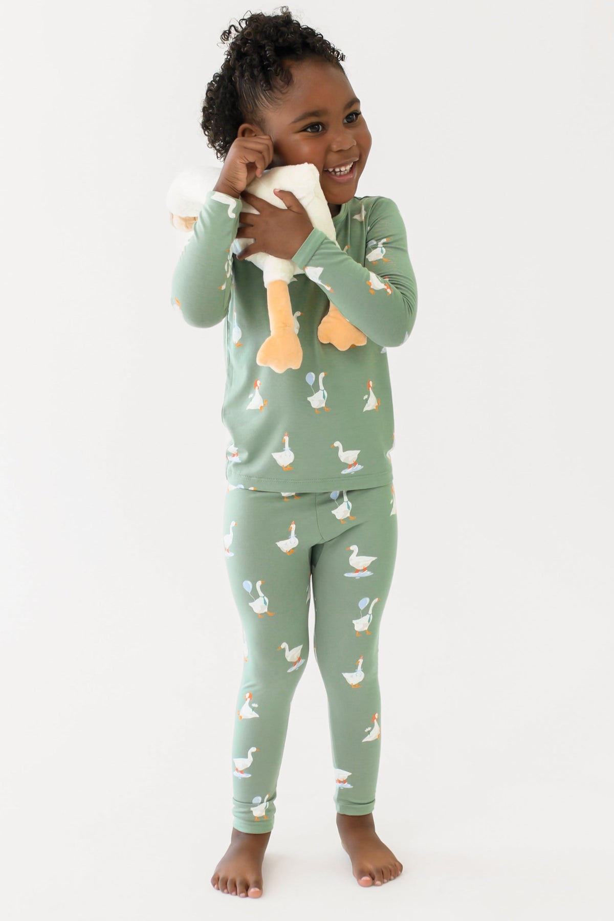 Smiling girl hugging a toy stuffed goose to her face wearing the Long Sleeve Pajamas in Silly Goose