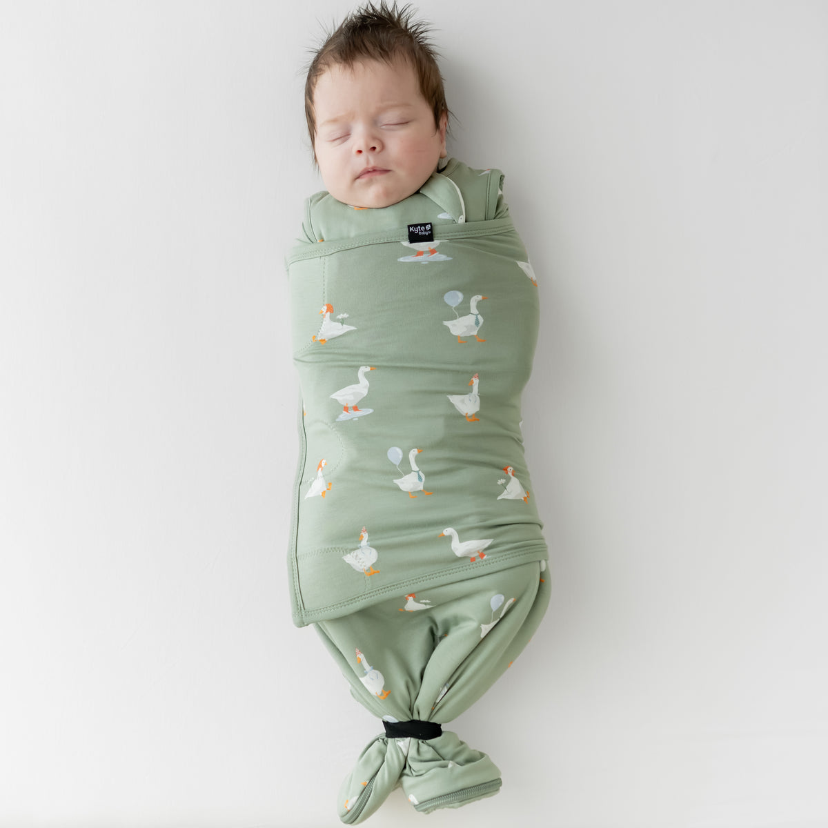 Sleeping newborn swaddled in the Sleep Bag Swaddler in Silly Goose 1.0 with the elastic band wrapping the bottom of the sleep bag