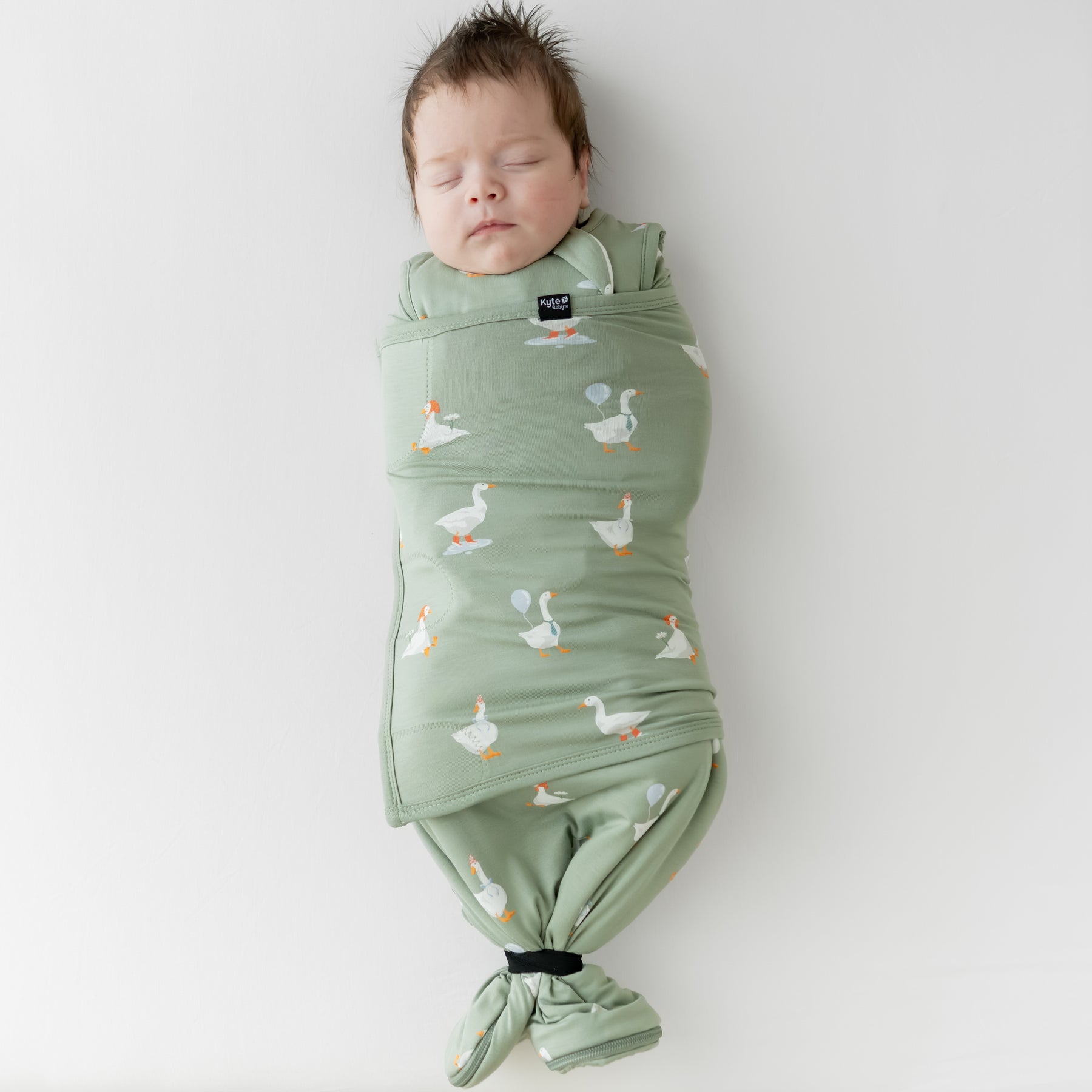 Sleeping newborn swaddled in the Sleep Bag Swaddler in Silly Goose 1.0 with the elastic band wrapping the bottom of the sleep bag
