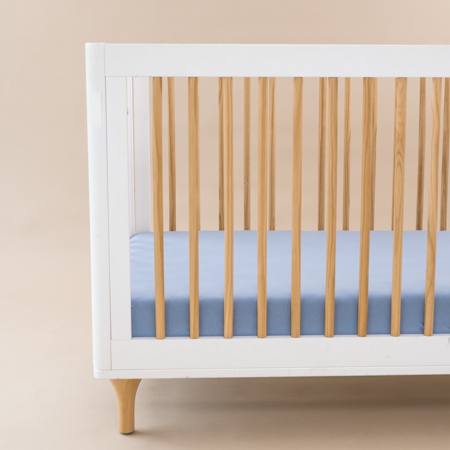 Crib Sheet in Slate shown on a mattress in a modern white and wooden crib