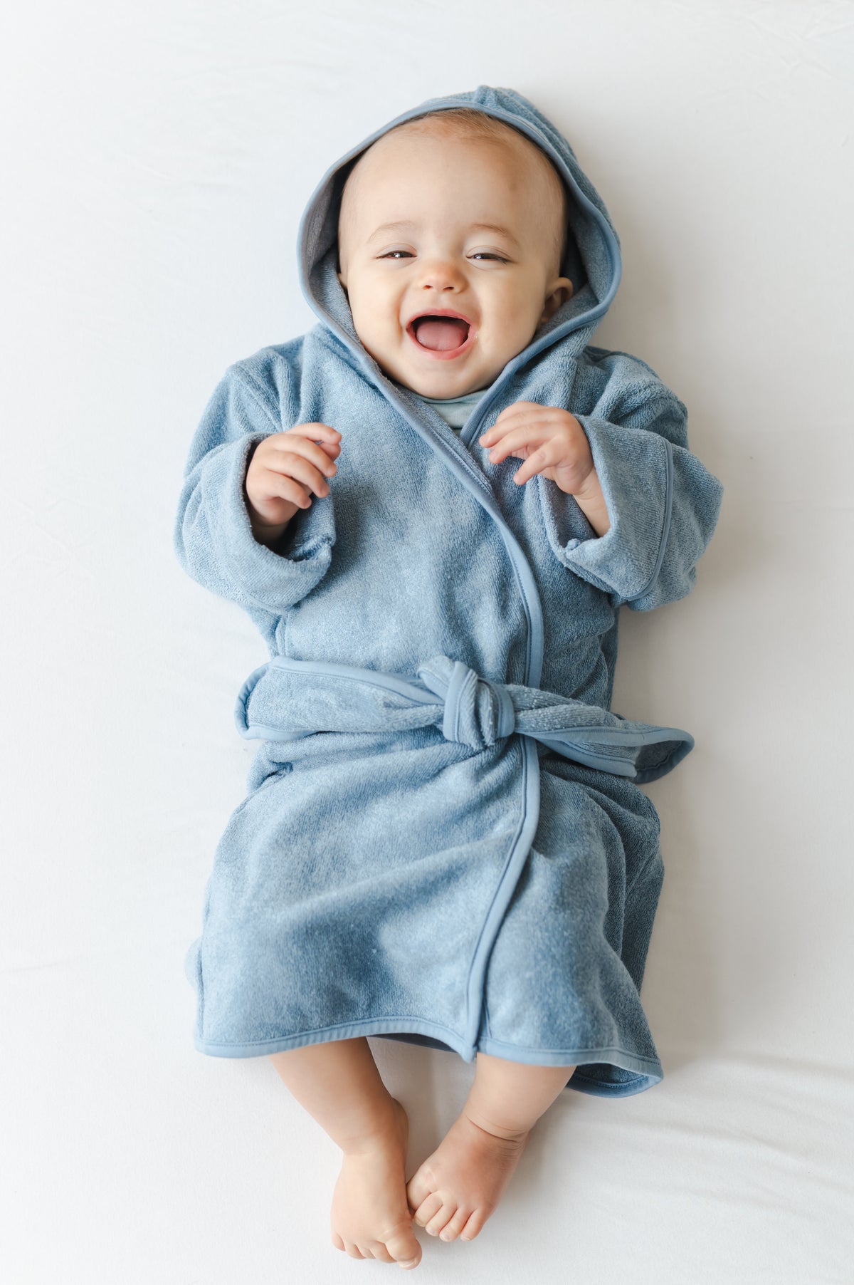 Smiling boy laying on a ed wearing the Hooded Bath Robe in Slate