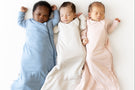 Three babies in colorful sleep bags lying on a white surface