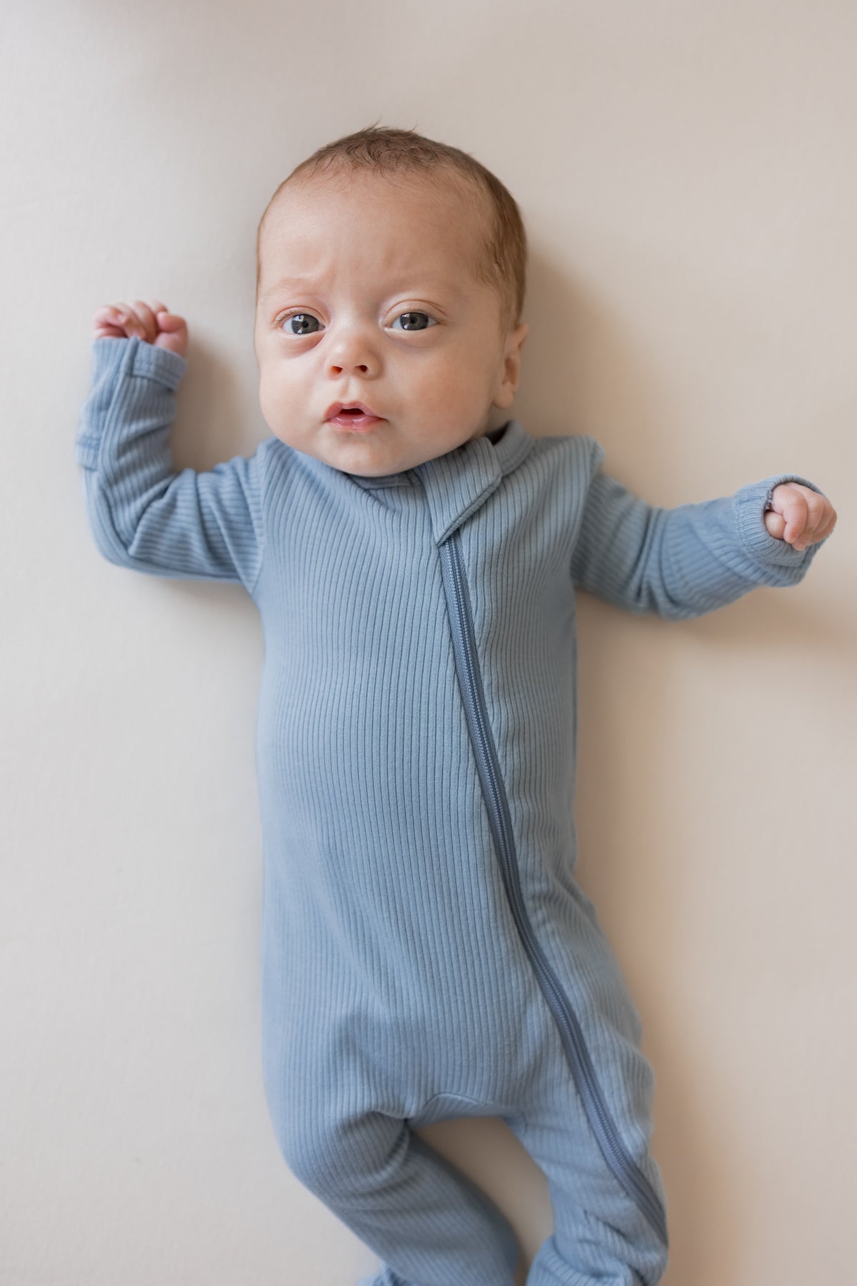 Close up of Baby wearing Ribbed Zippered Romper in Slate color on a beige background
