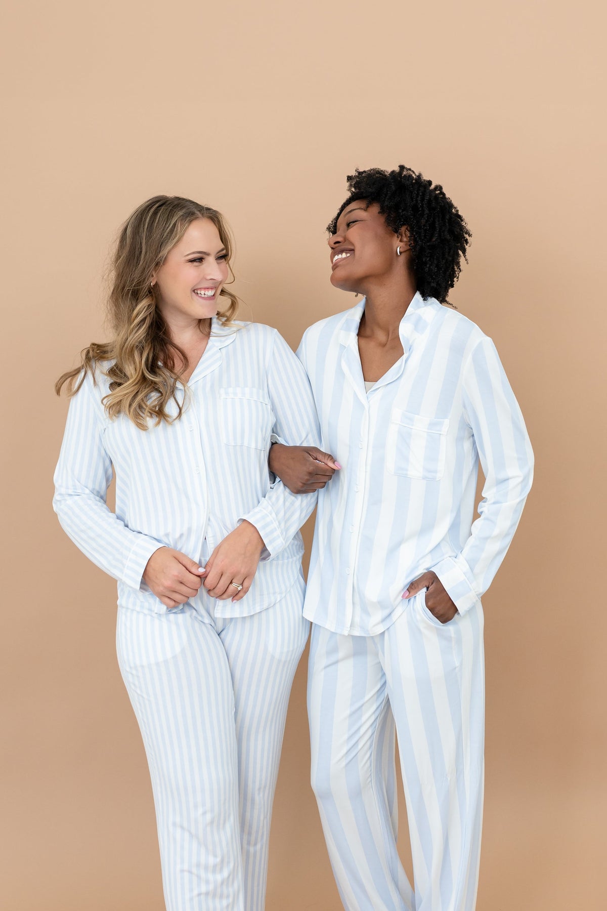 Two smiling female models standing side by side with their arms locked wearing the Long-Sleeved Women's Pajama Set in Small Mist Stripe and Big Mist Stripe