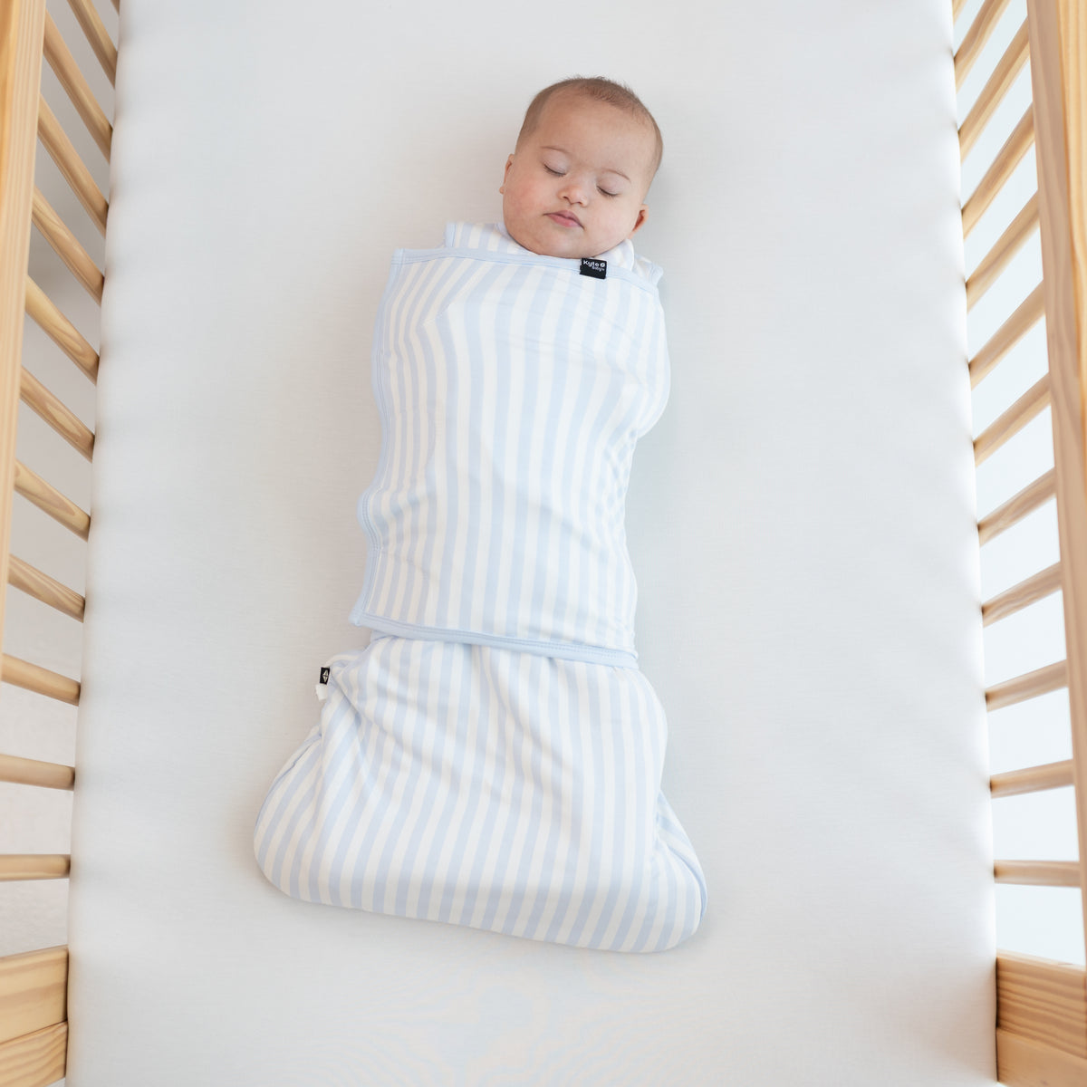 Sleeping Baby laying in a crib swaddled in the Sleep Bag Swaddler in Small Mist Stripe 1.0