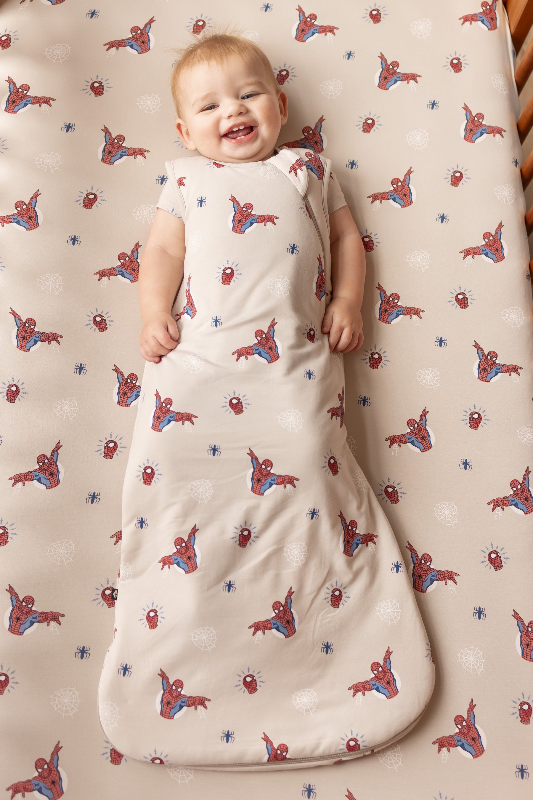 Baby in oat color Sleep Bag with Spider-Man print lying on a similar print crib sheet.