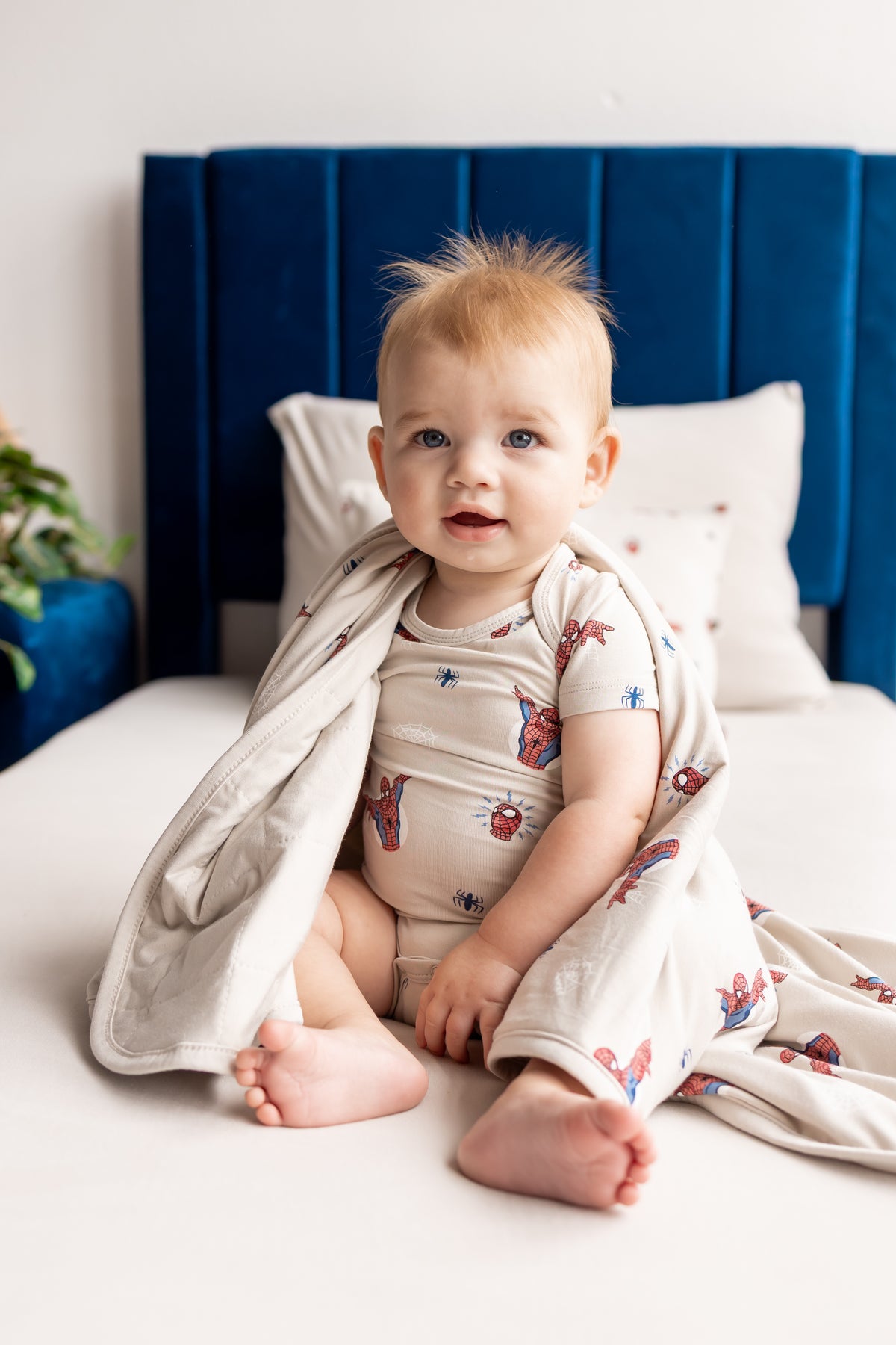 Baby posing on a beige bed wrapped in an oat color Baby Blanket with Spider-Man print