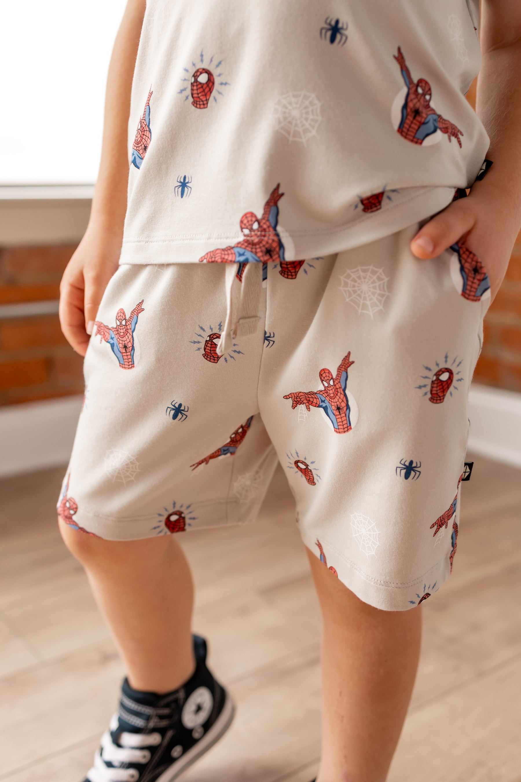 Boy wearing oat color Toddler Drawstring shorts under Toddler basic tee with Spider-Man print in front of a brick wall