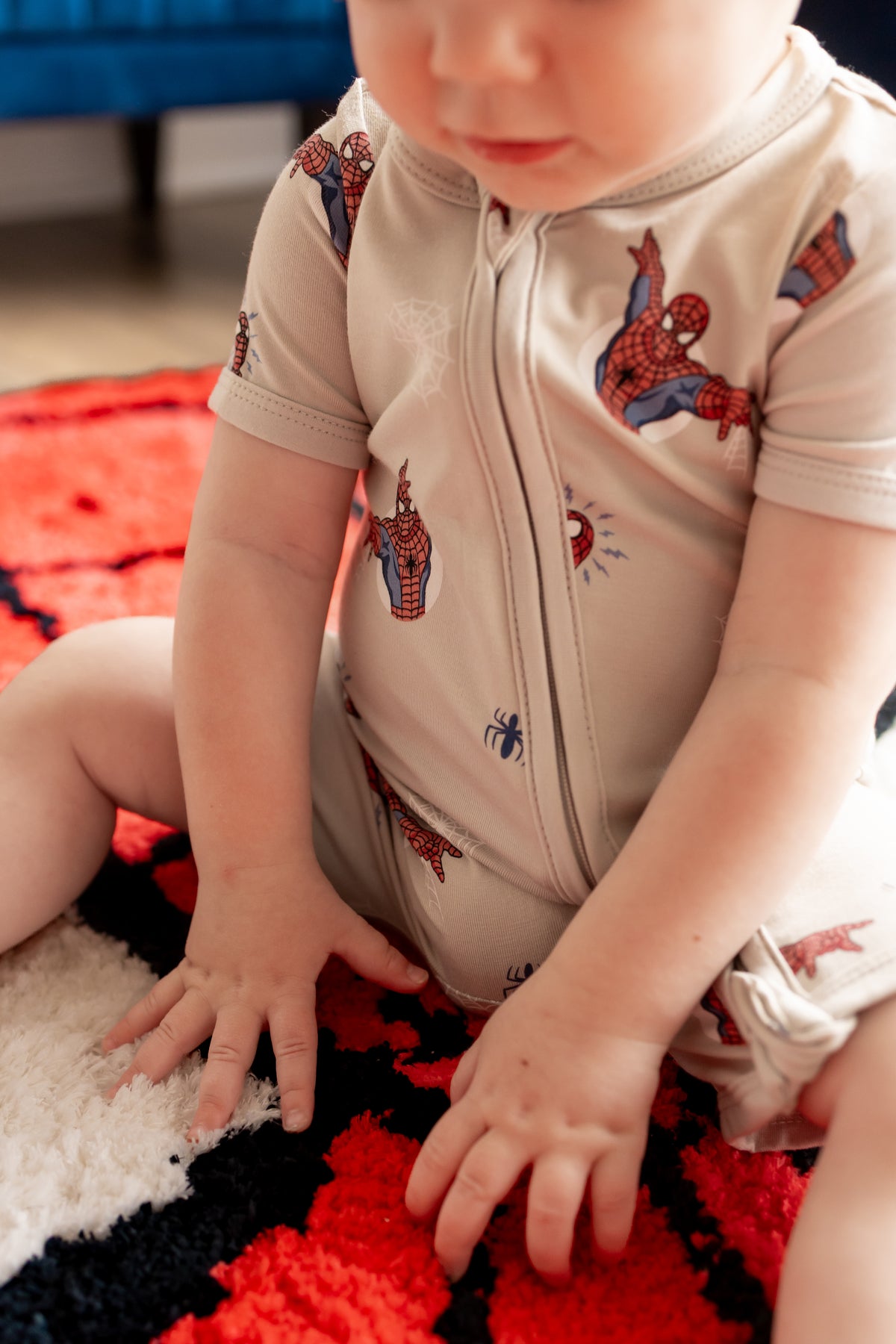 Toddler sitting in spider man print rug wearing oat color Zipper Shortall Romper with Spider-Man print