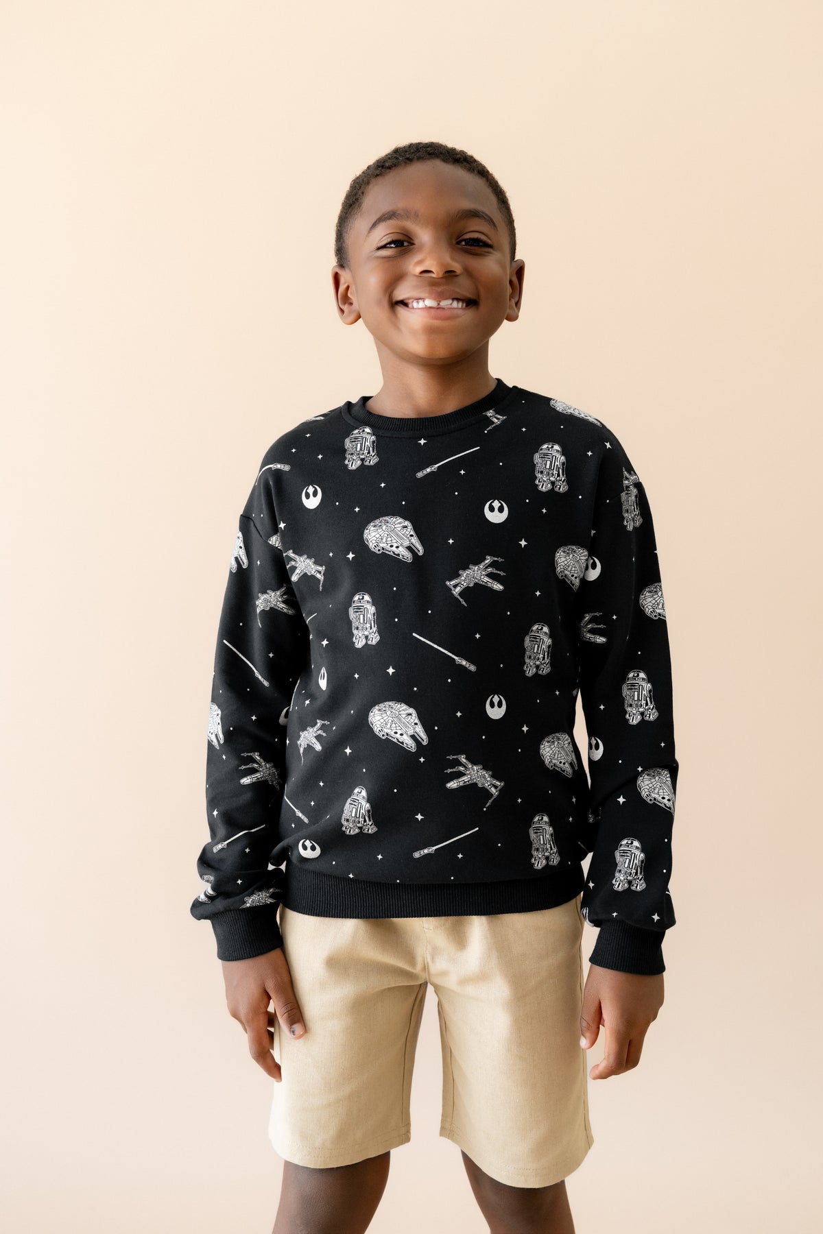 Smiling boy wearing the Sweatshirt in STAR WARS™ paired with tan shorts