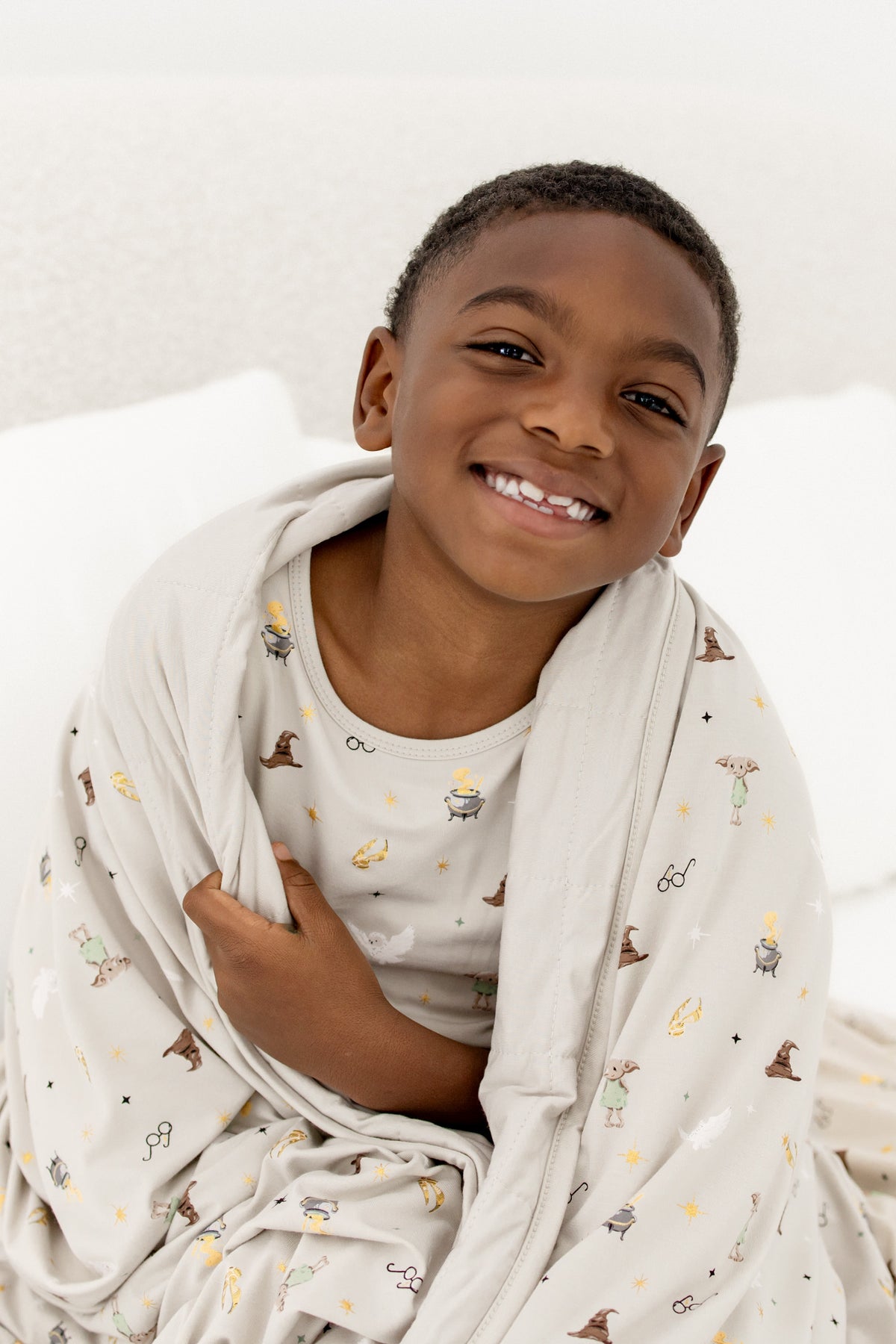 Child wrapped in a beige Youth blanket with Harry Potter prints wearing a similar print shirt on a beige background