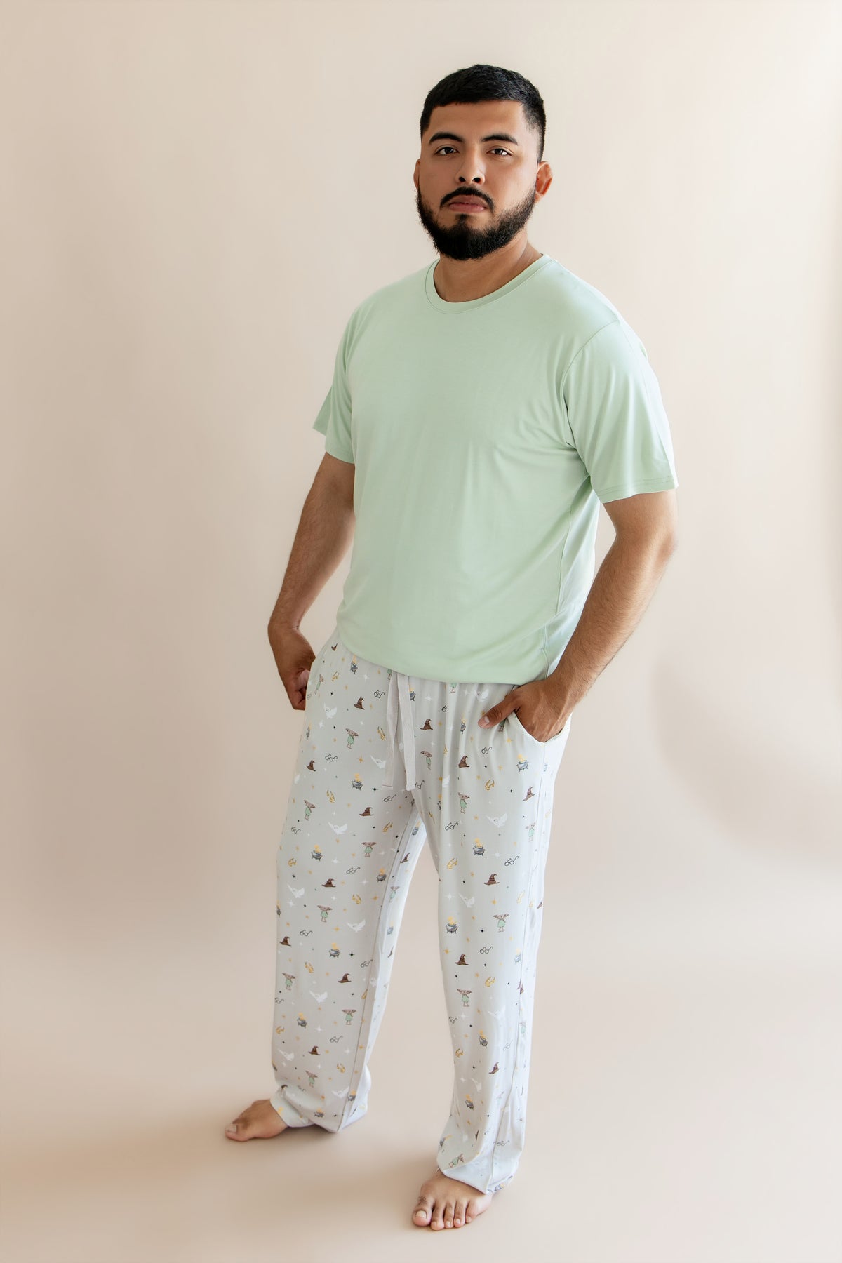 Person wearing a cream men's lounge pant with Harry Potter prints with green shirt on a beige background