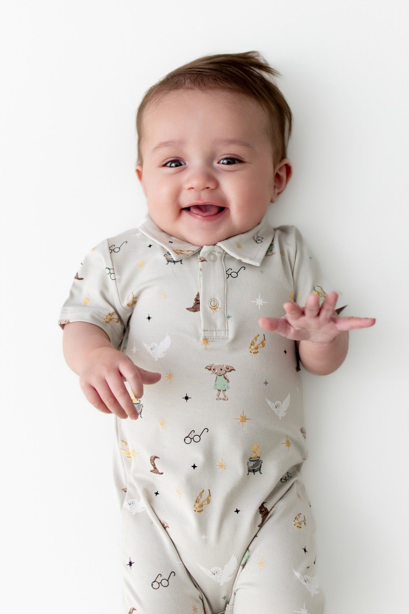 Baby wearing a cream polo shortall with Harry Potter prints on a white background